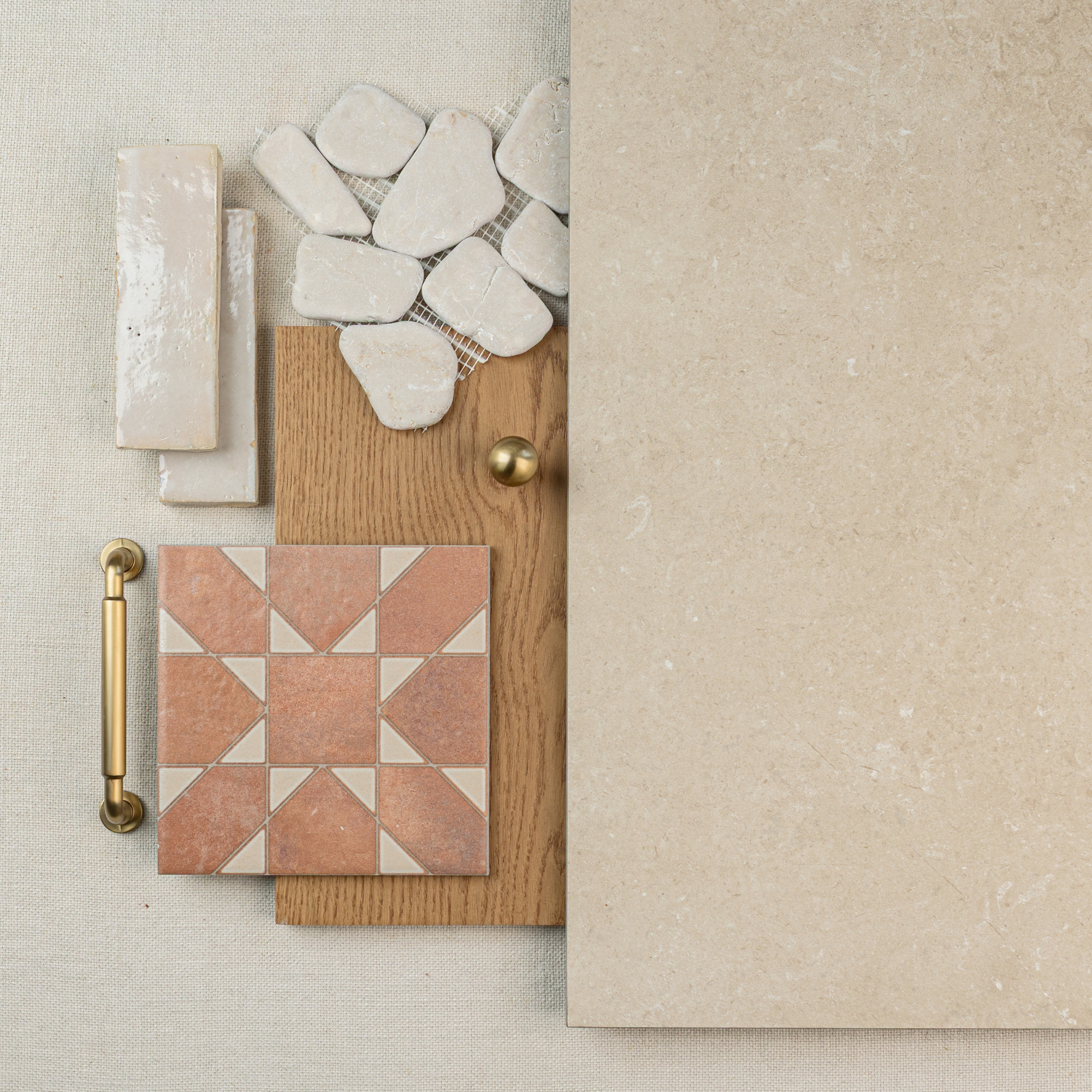 Flat lay of beige stone tile, terracotta patterned ceramic tile, irregular white mosaic, wood plank, and brass hardware on neutral fabric