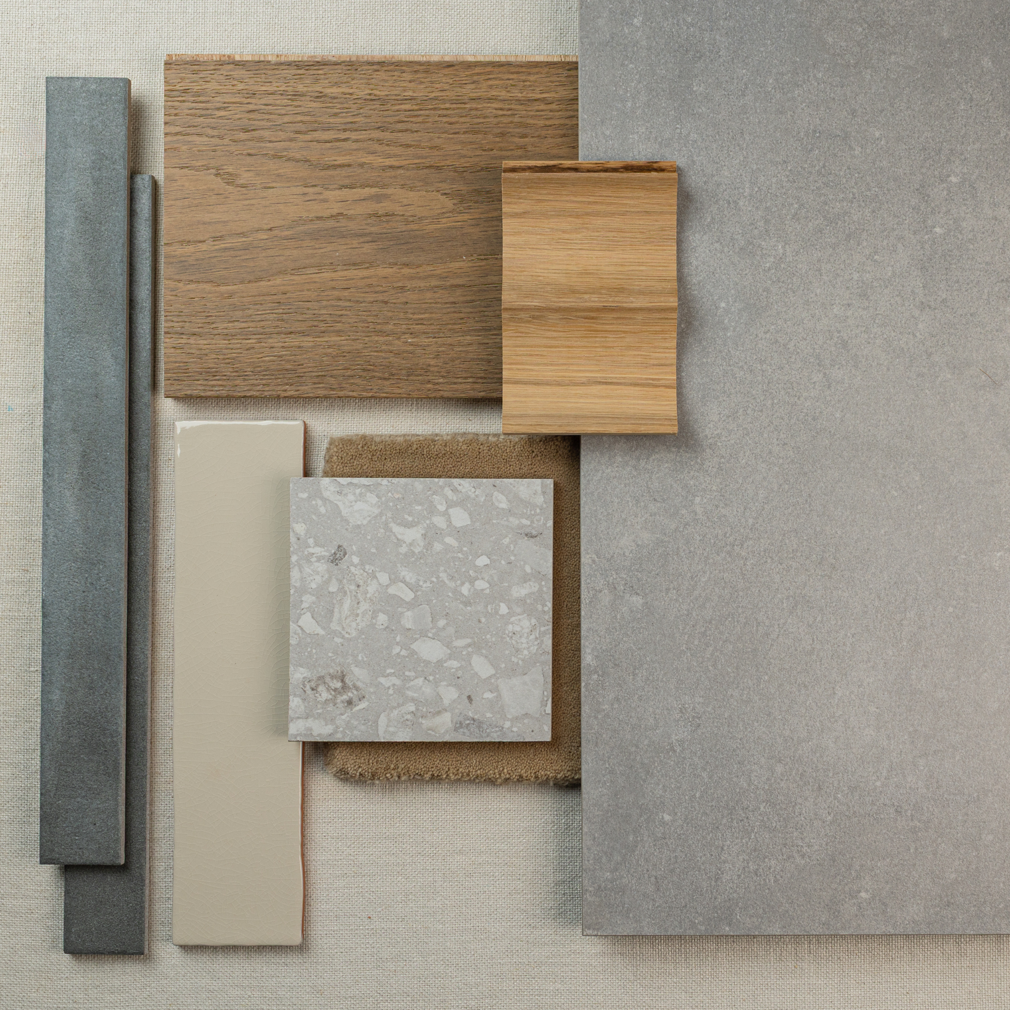Arrangement of ash cement-look large format tile, wood samples, beige ceramic tile, concrete-look tile, and neutral fabric swatch