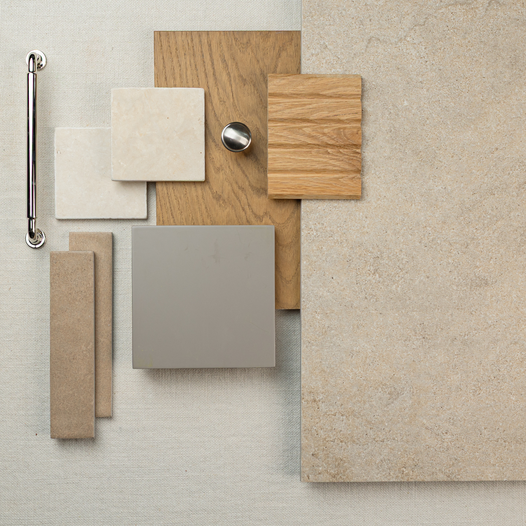 Overhead view of beige large format tile, wood samples, small stone tiles, and silver cabinet knob on neutral fabric background