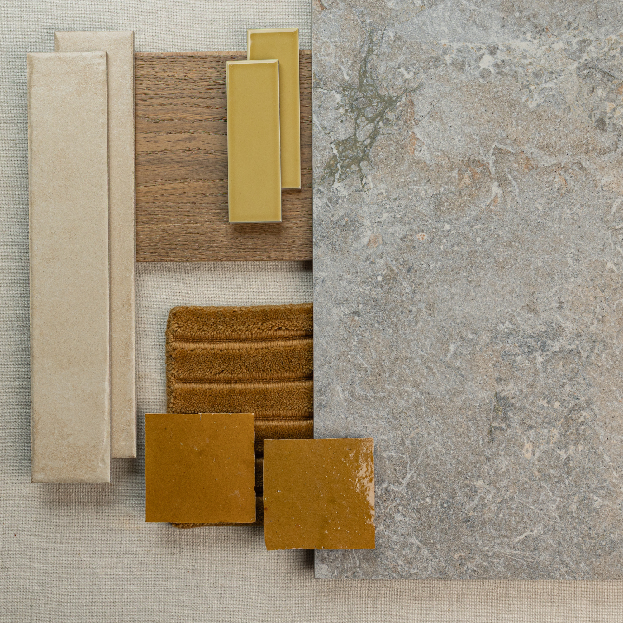 Flat lay of neutral large format stone-look tile with beige ceramic, mustard yellow tiles, textured wood, and fabric samples