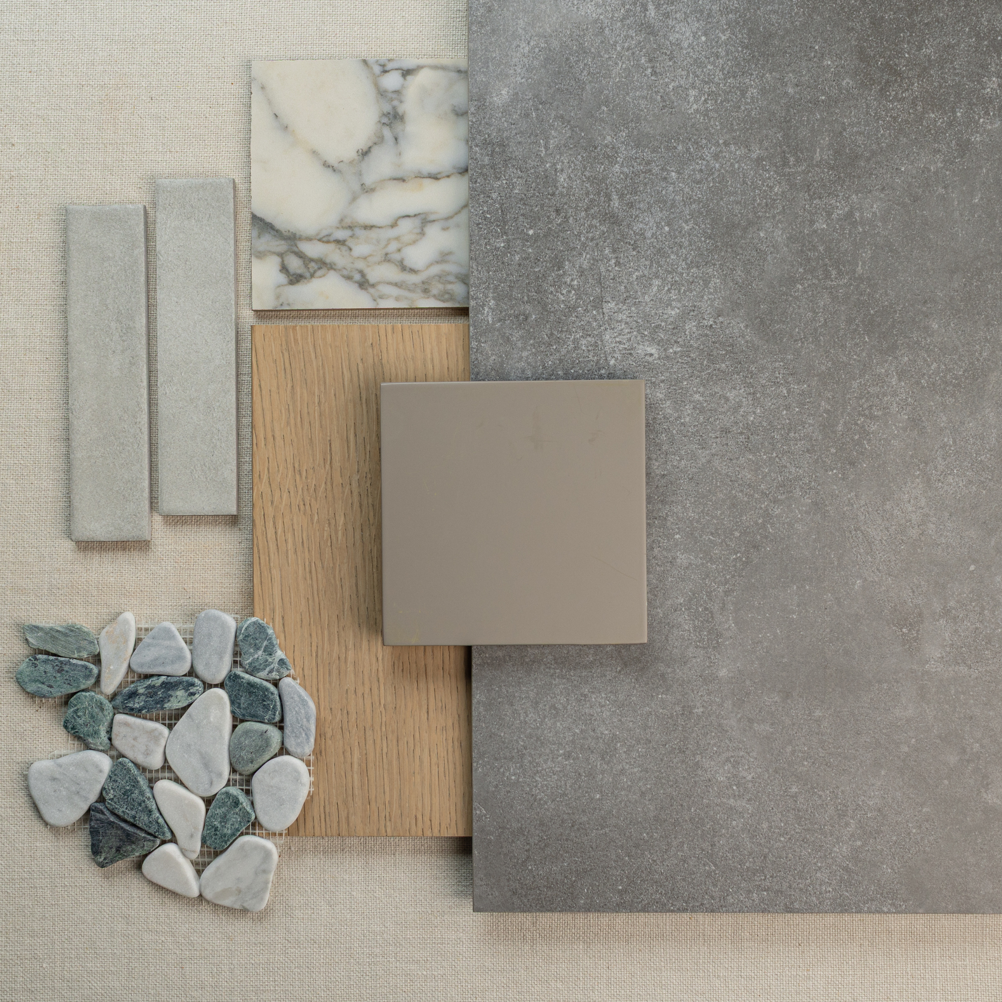 Assorted grey stone tile, marble slab, wood sample, smooth paint swatch, and mixed pebble mosaic on neutral fabric
