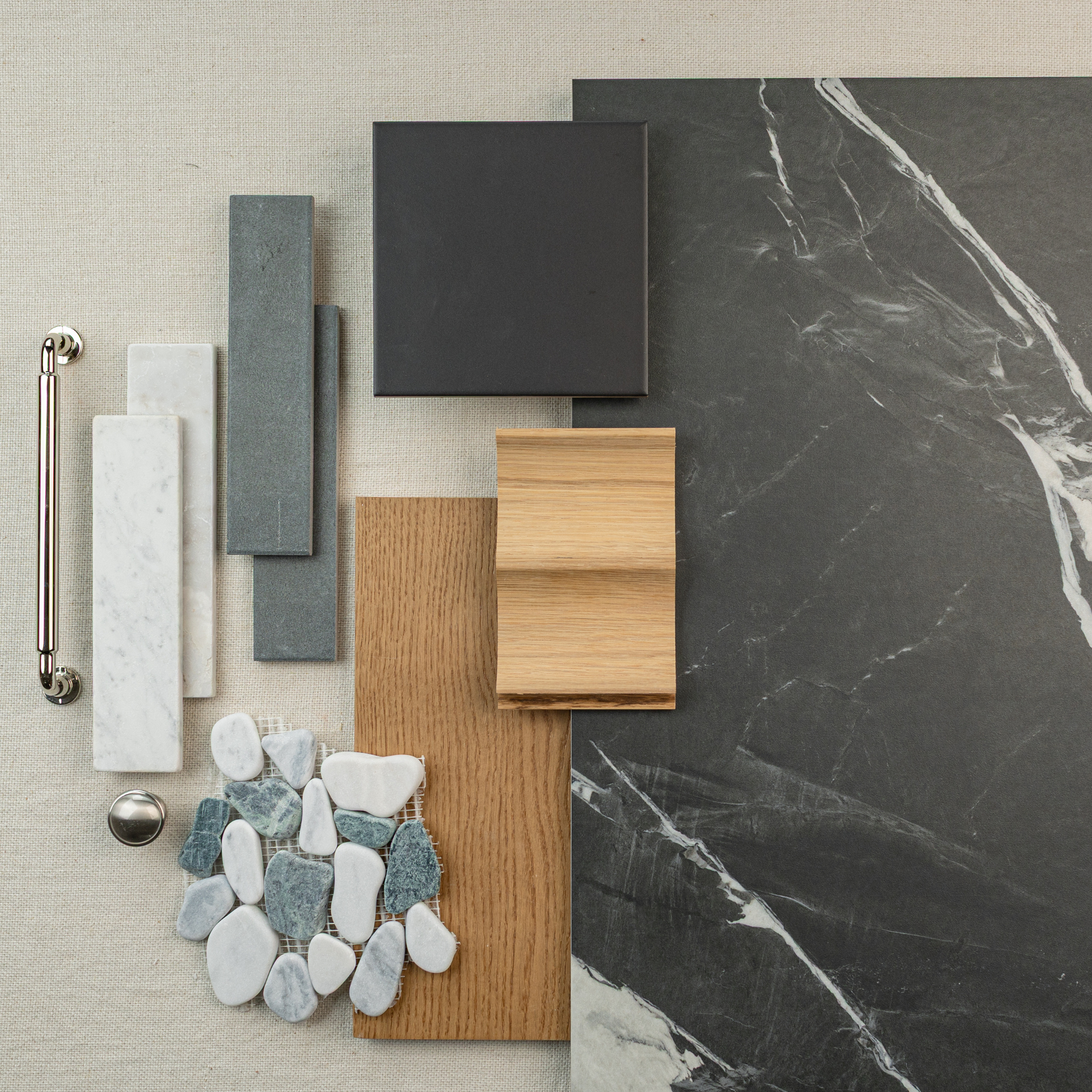 Collection of dark large format tiles, wood samples, blue and white stone mosaic, metal hardware on light neutral fabric background