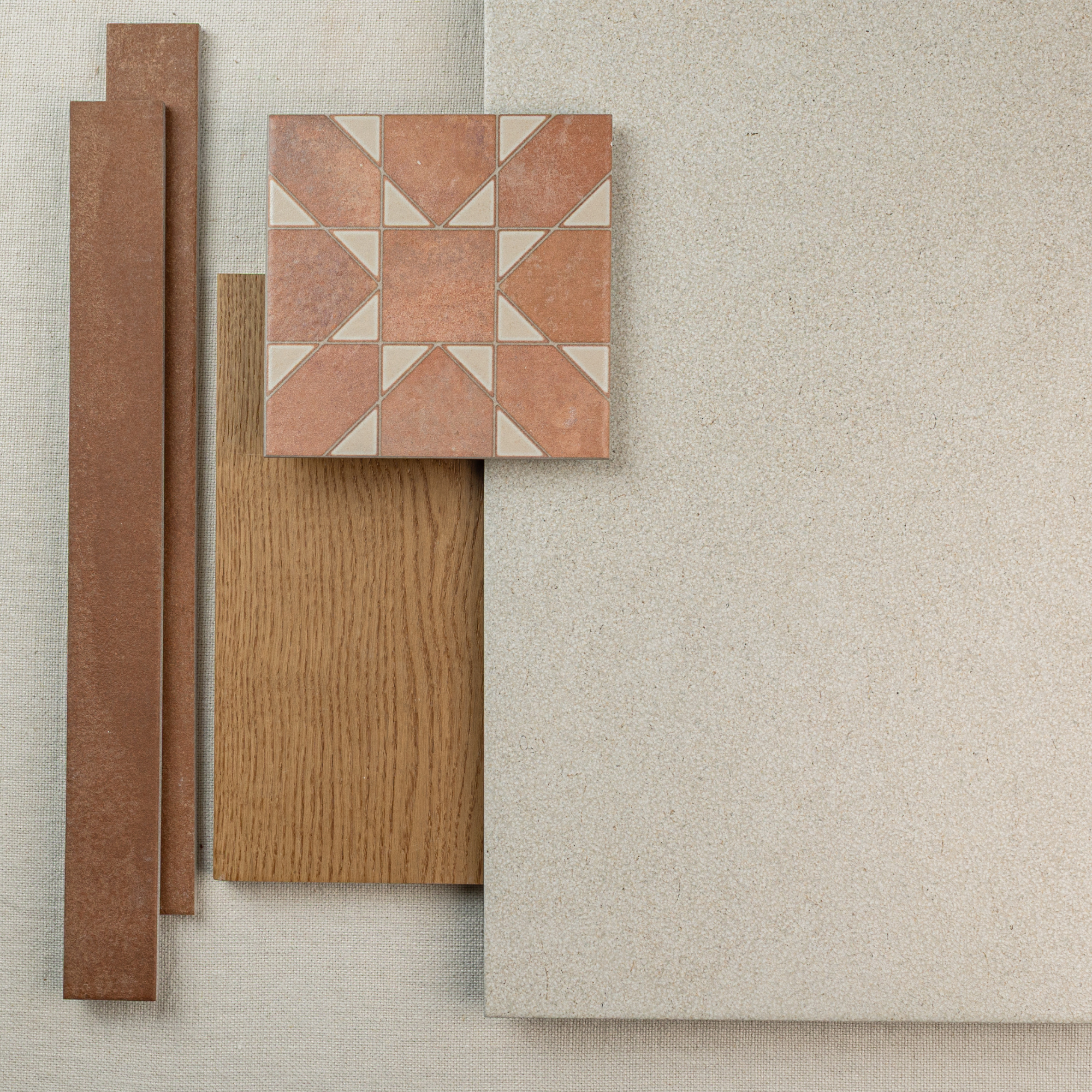 Overhead view of terracotta patterned tile, wood plank, rust-colored trim, and large neutral stone tile arranged on fabric background