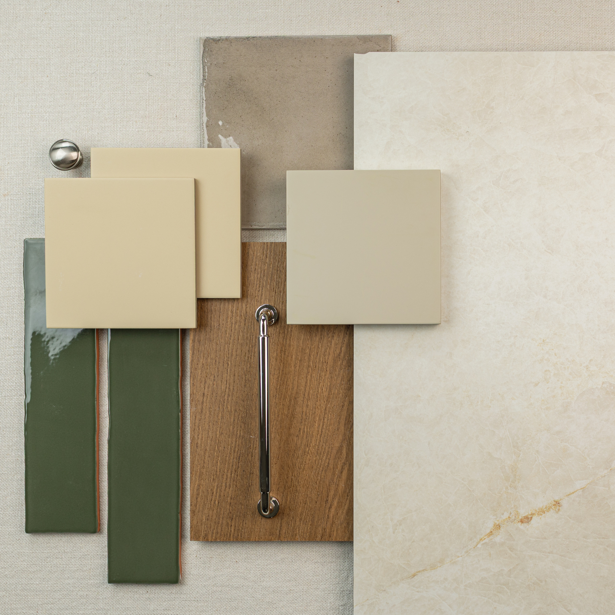 Arrangement of ceramic tiles in cream, beige, green, taupe, wood sample, and a metal handle on fabric background