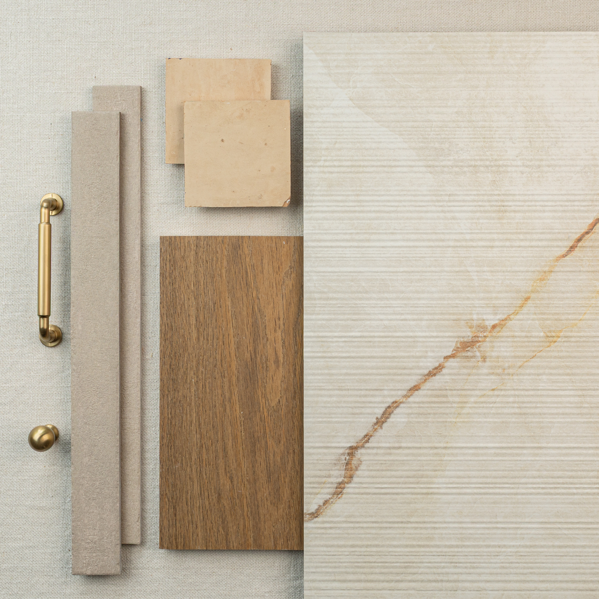 Flat lay of large cream textured tile with wood and beige ceramic samples alongside brass hardware on fabric backdrop