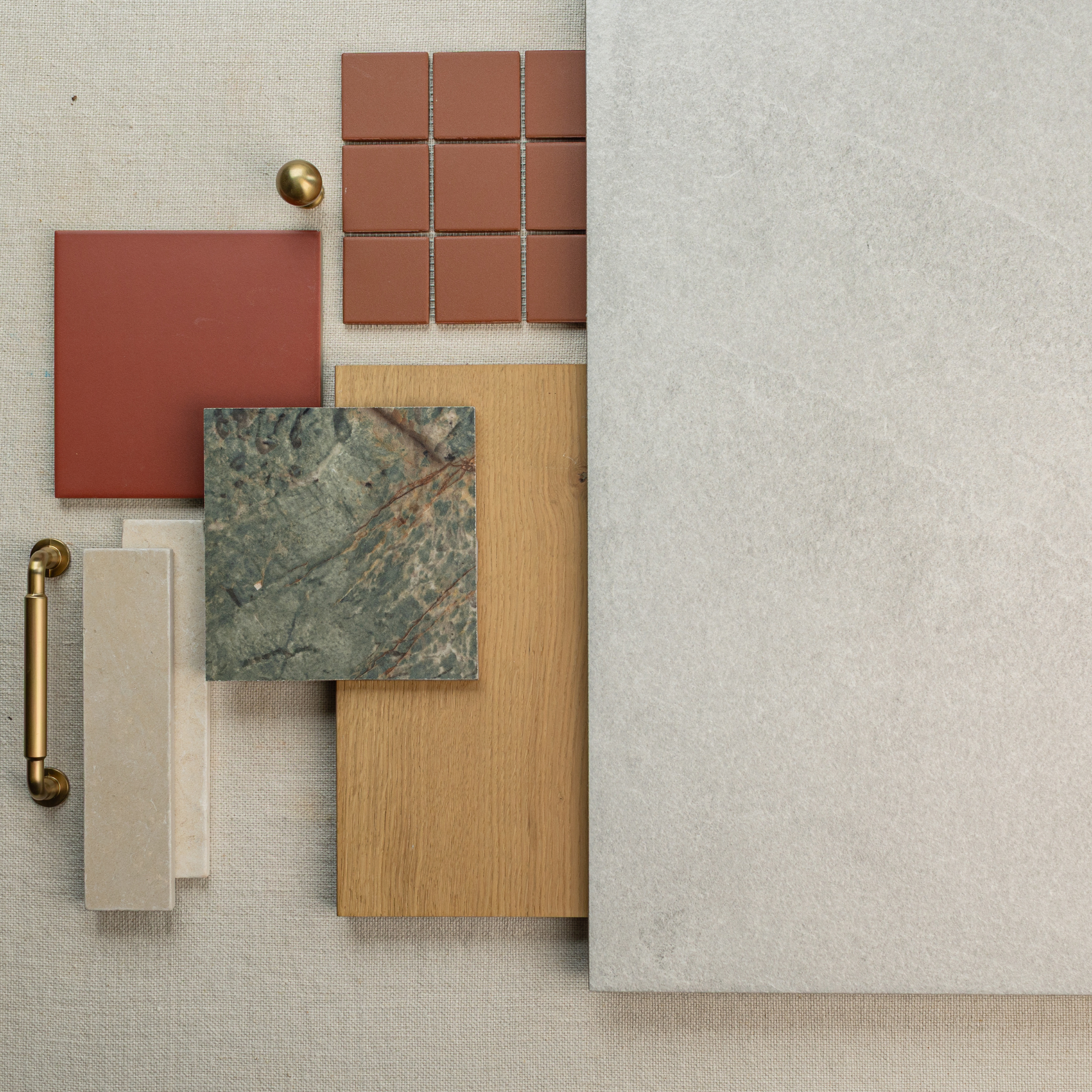 Arrangement of terracotta, green stone, beige and oak wood samples with brass handle and large light gray tile on linen background