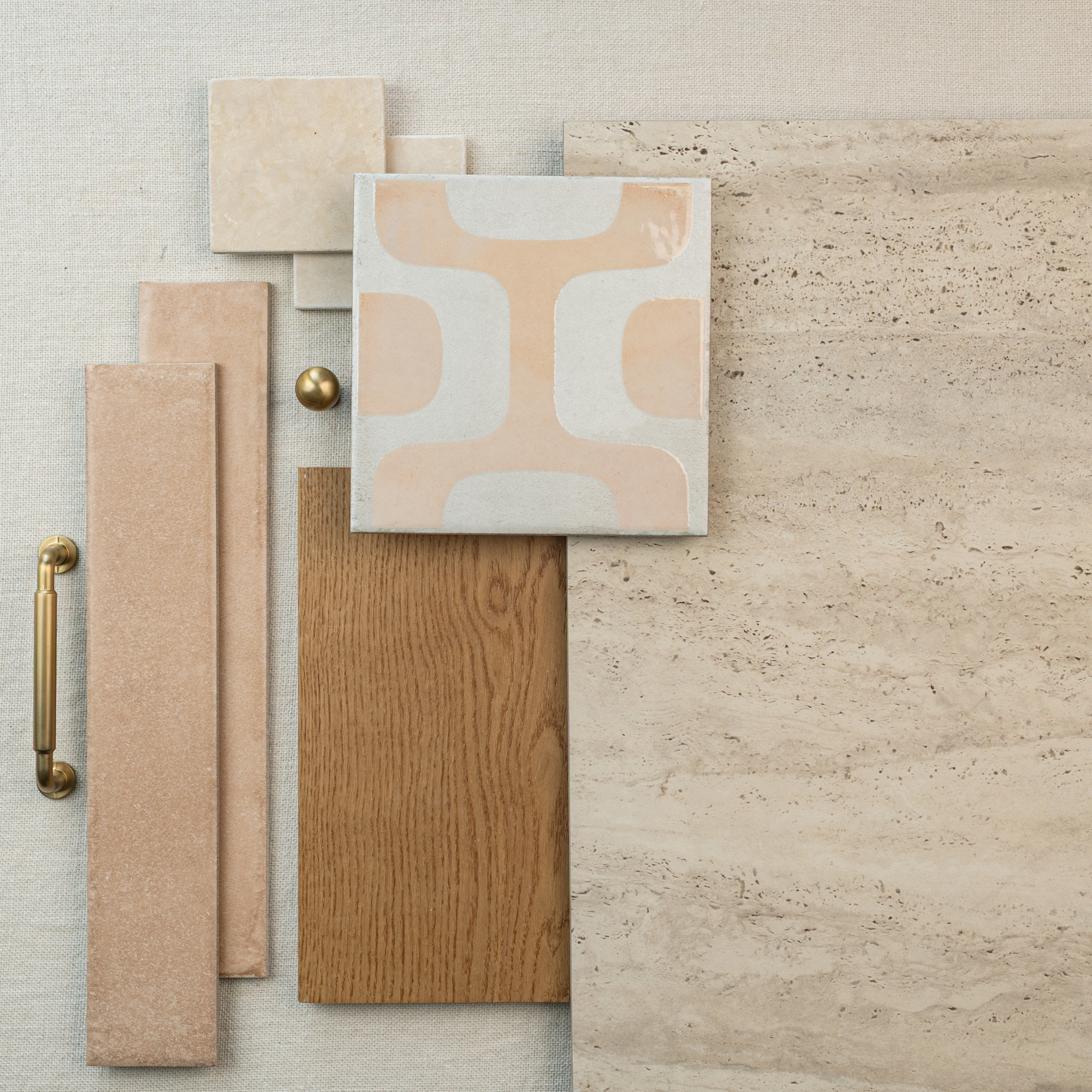 Assorted tiles, wood samples, and brass hardware arranged flat on a neutral fabric background in warm beige tones