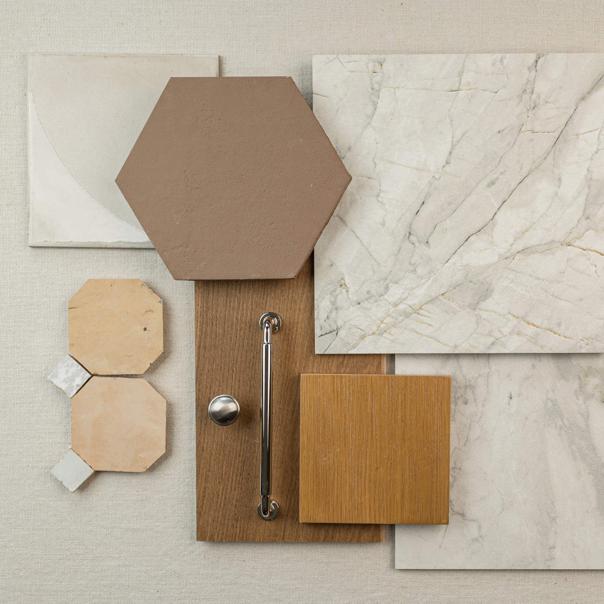 Assortment of ceramic and wood flooring samples including hexagonal, square, and marble-effect tiles with a metallic handle accent