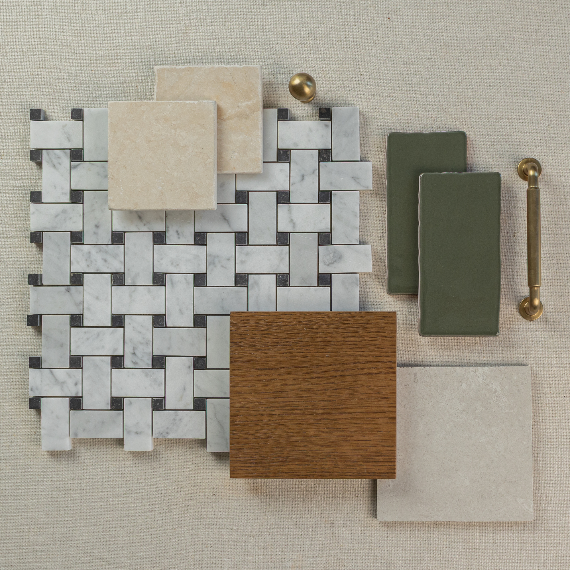 Flat lay of white and gray marble basketweave mosaic tile with beige stone, green ceramic tiles, wood plank, and brass hardware on fabric