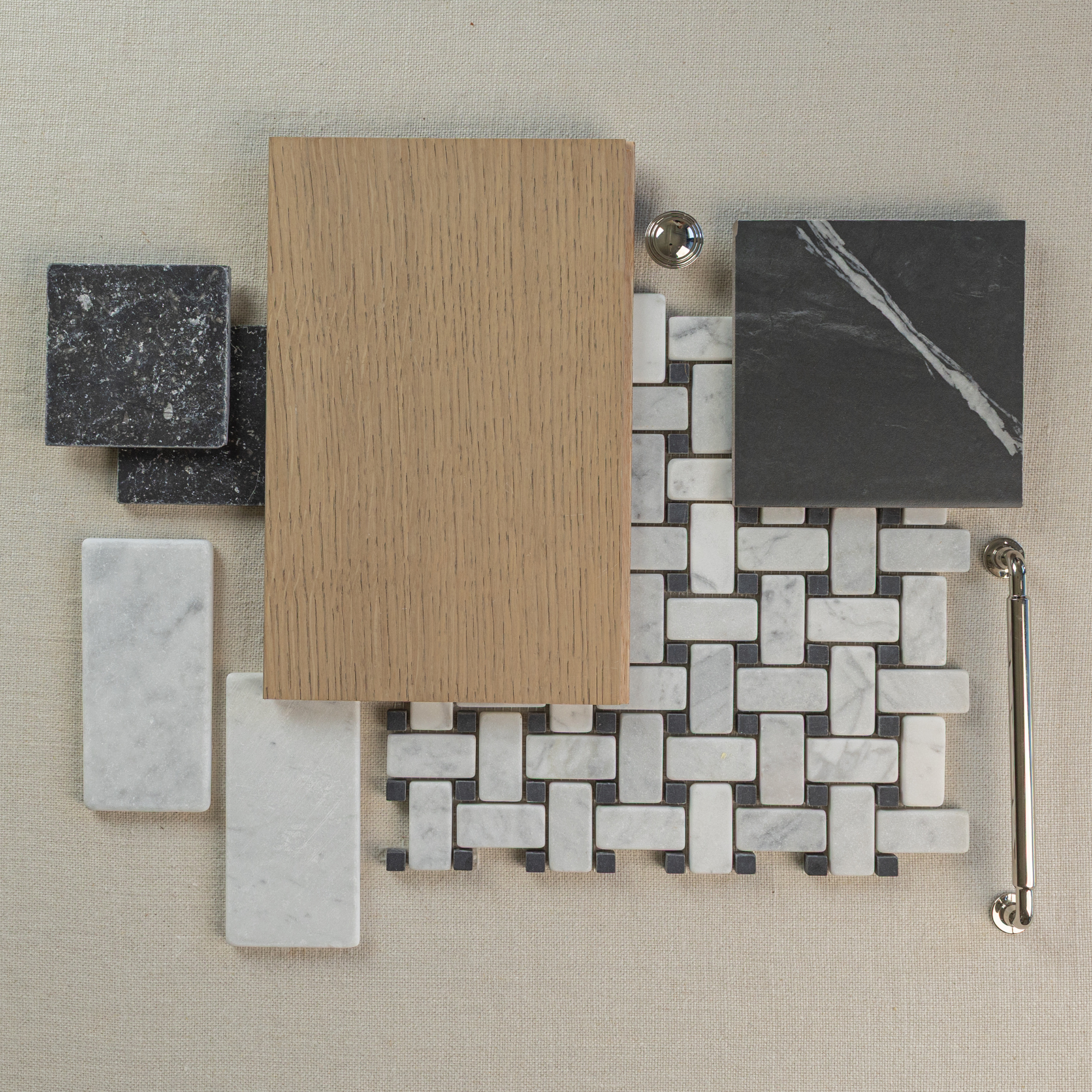 Flat lay of marble mosaic tiles, oak wood plank, dark stone tile, white rectangular tiles, and brass hardware on neutral fabric