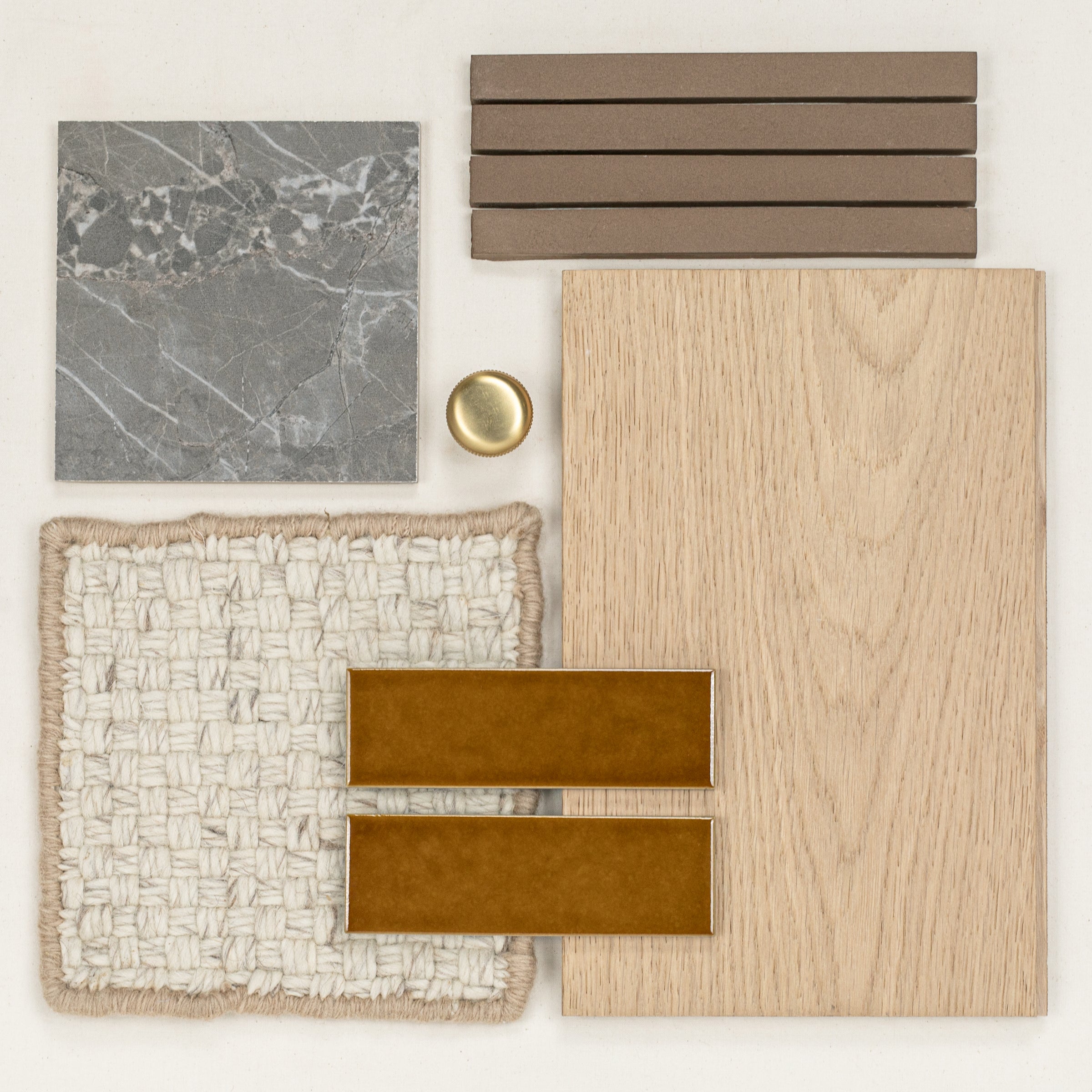 Flat lay of natural wood veneer, gray stone tile, tan ceramic strips, textured cream fabric, amber ceramic tiles, and a brass knob