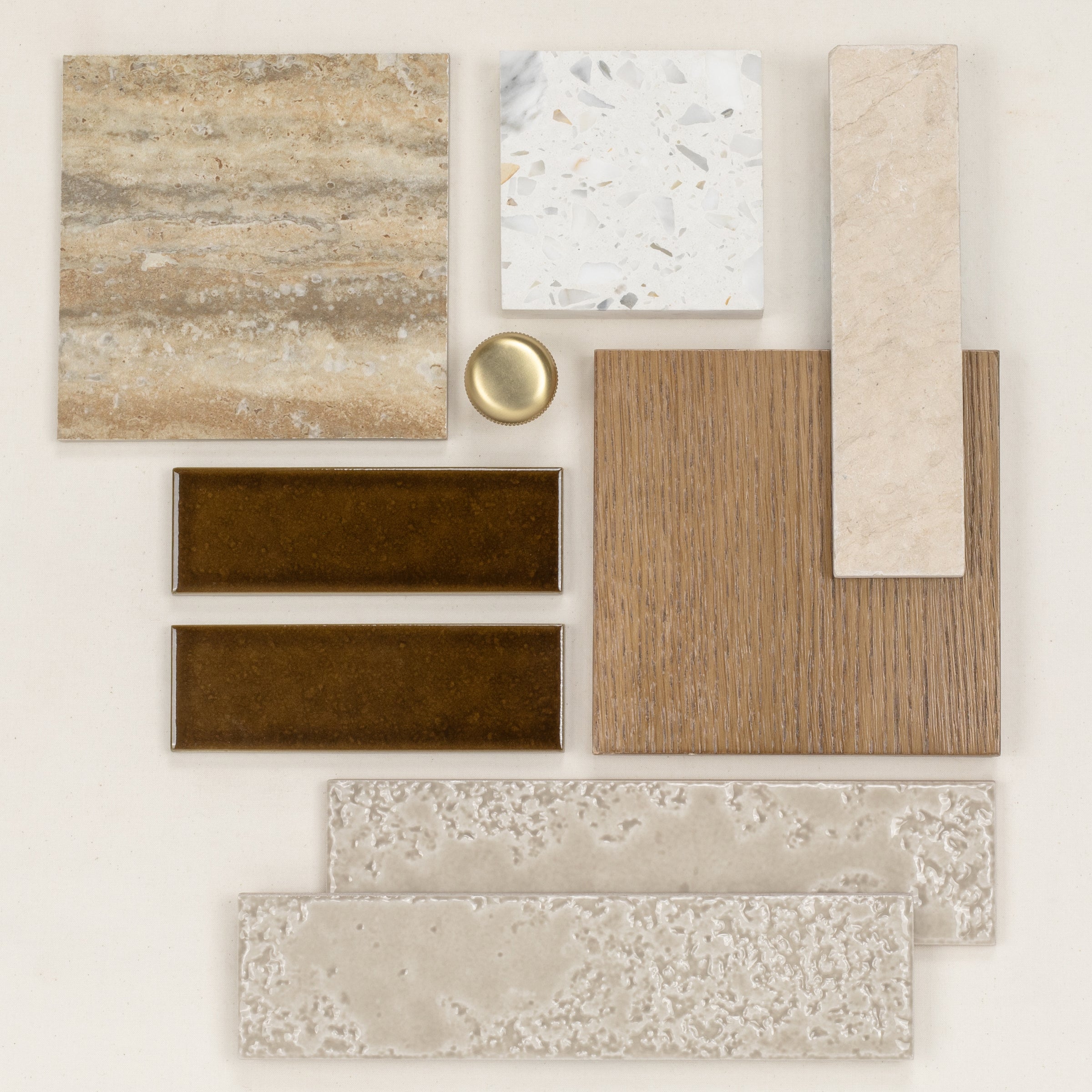 Assortment of neutral ceramic and porcelain tiles with wood and brass accents arranged on a light background