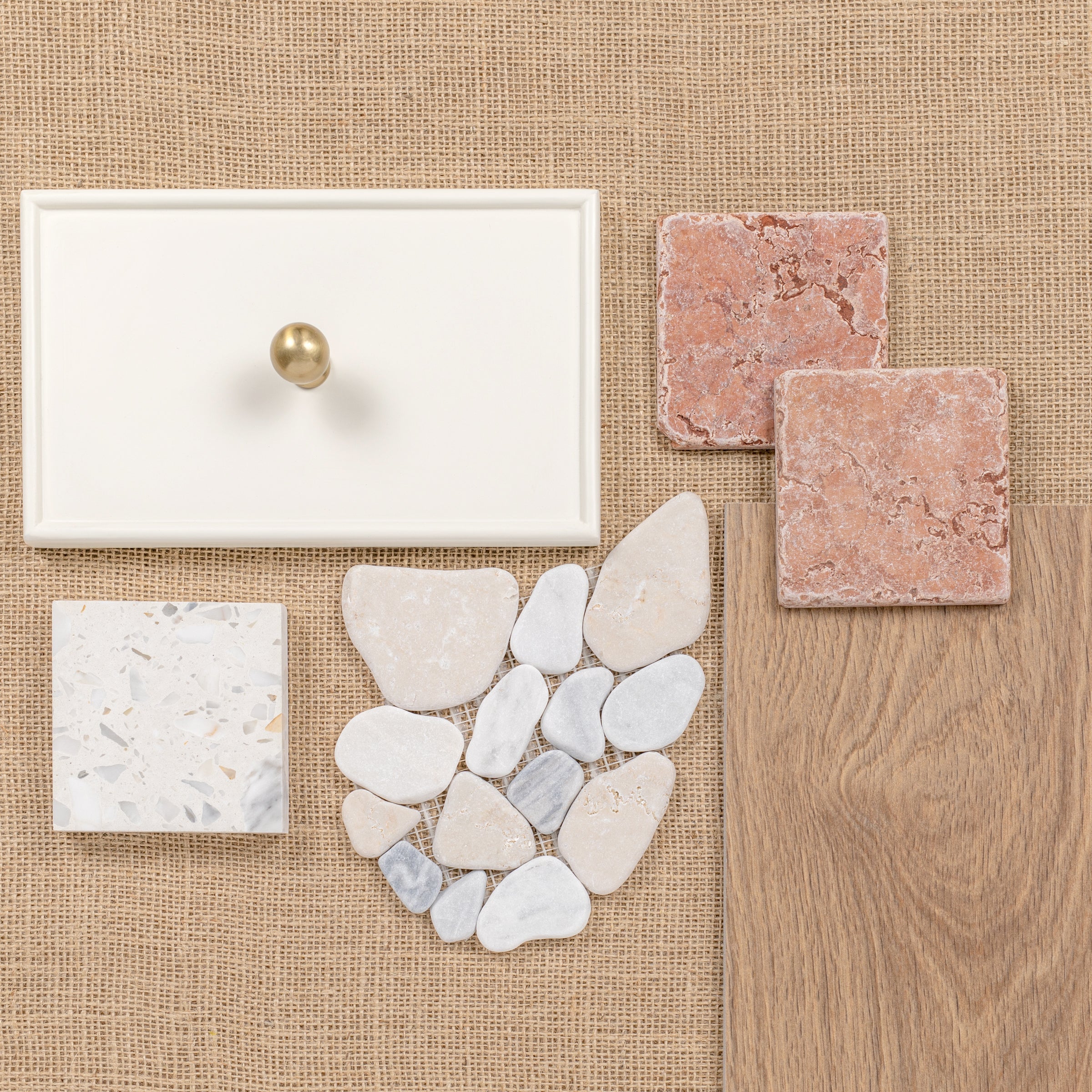 Flat lay of cabinet knob, stone tiles, pebbles, and wood flooring samples on burlap background