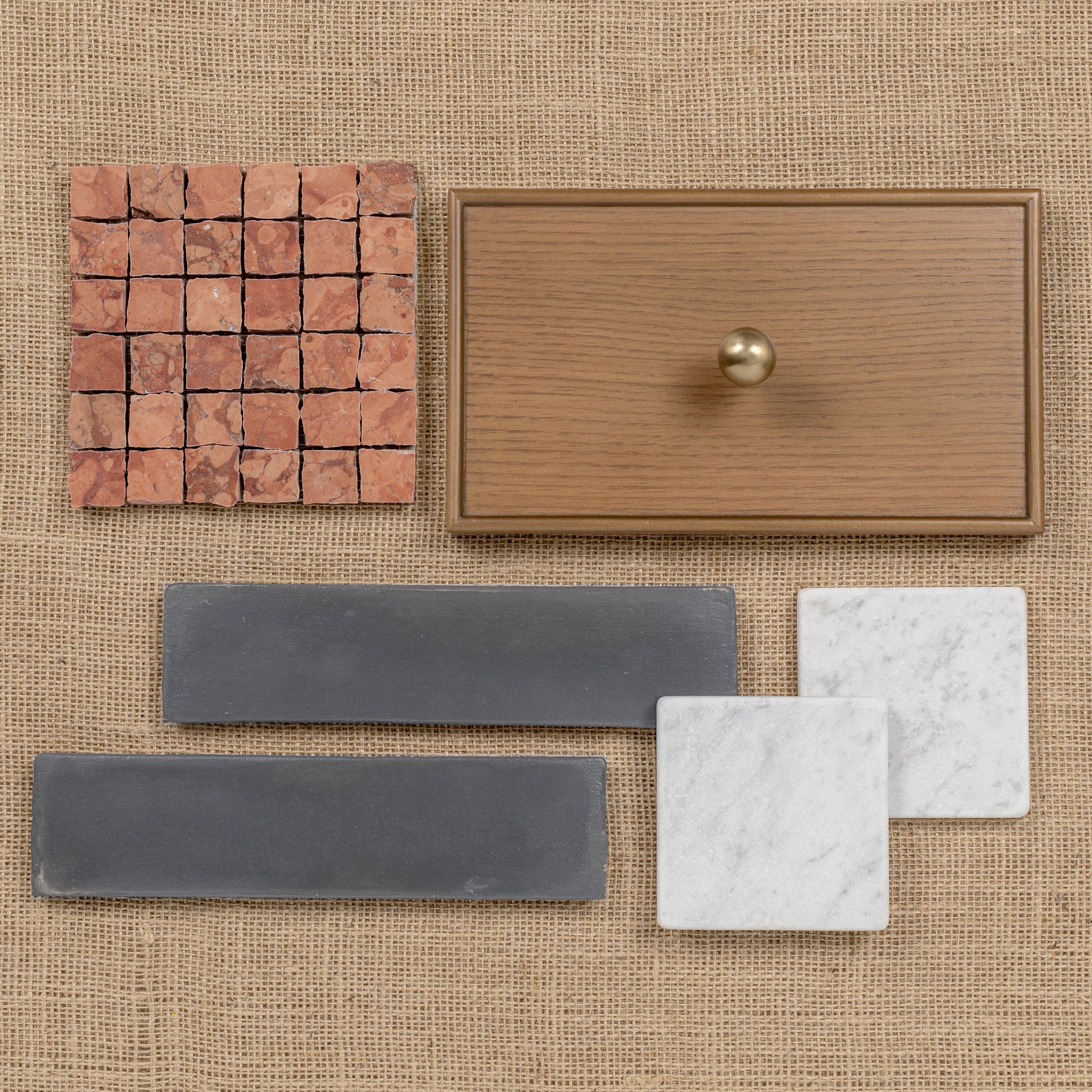 Assortment of terracotta tiles, oak drawer front with knob, porcelain tile strips, and marble square tiles on burlap.