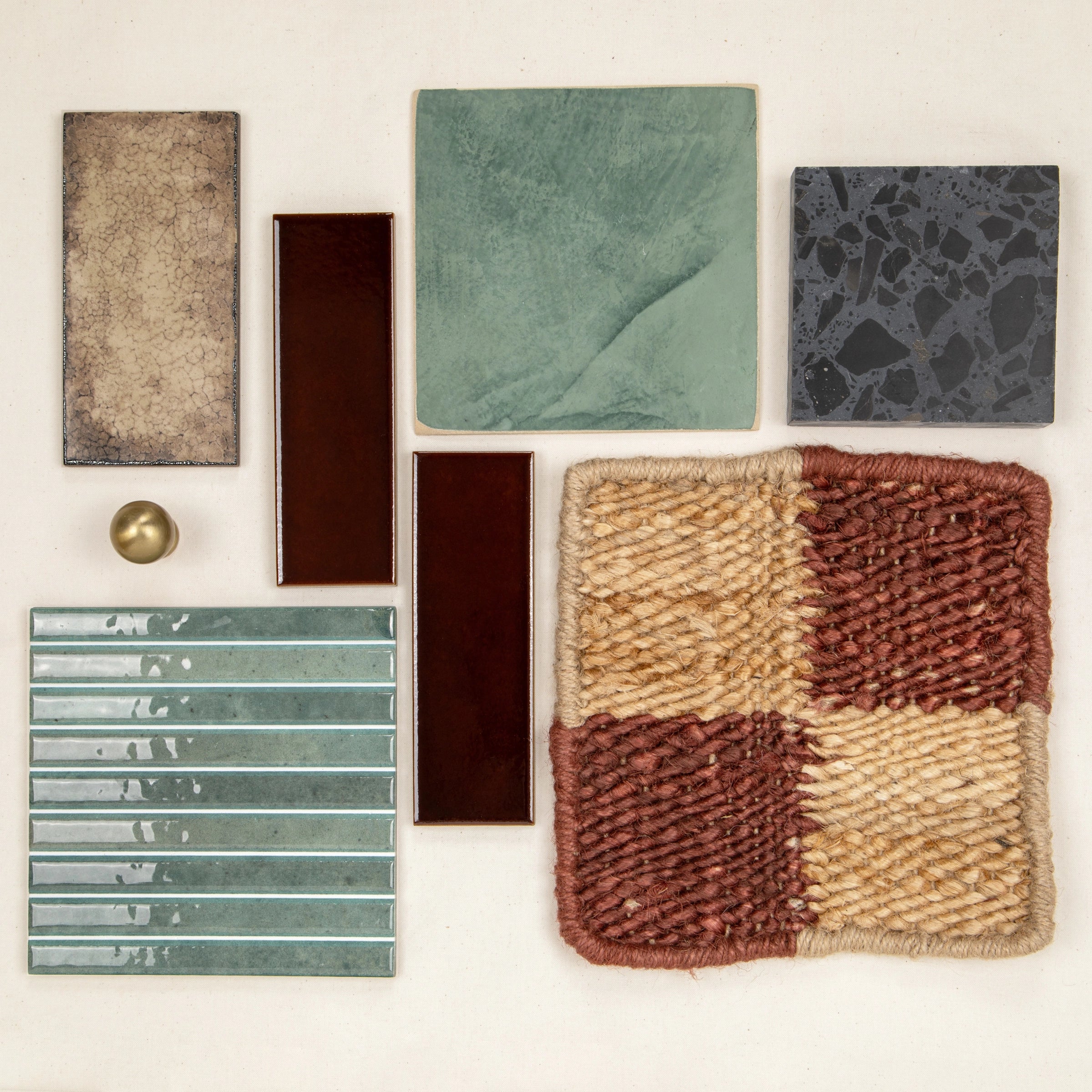 Assortment of ceramic, porcelain, and textured tiles in earthy tones arranged with a woven textile swatch and a brass knob