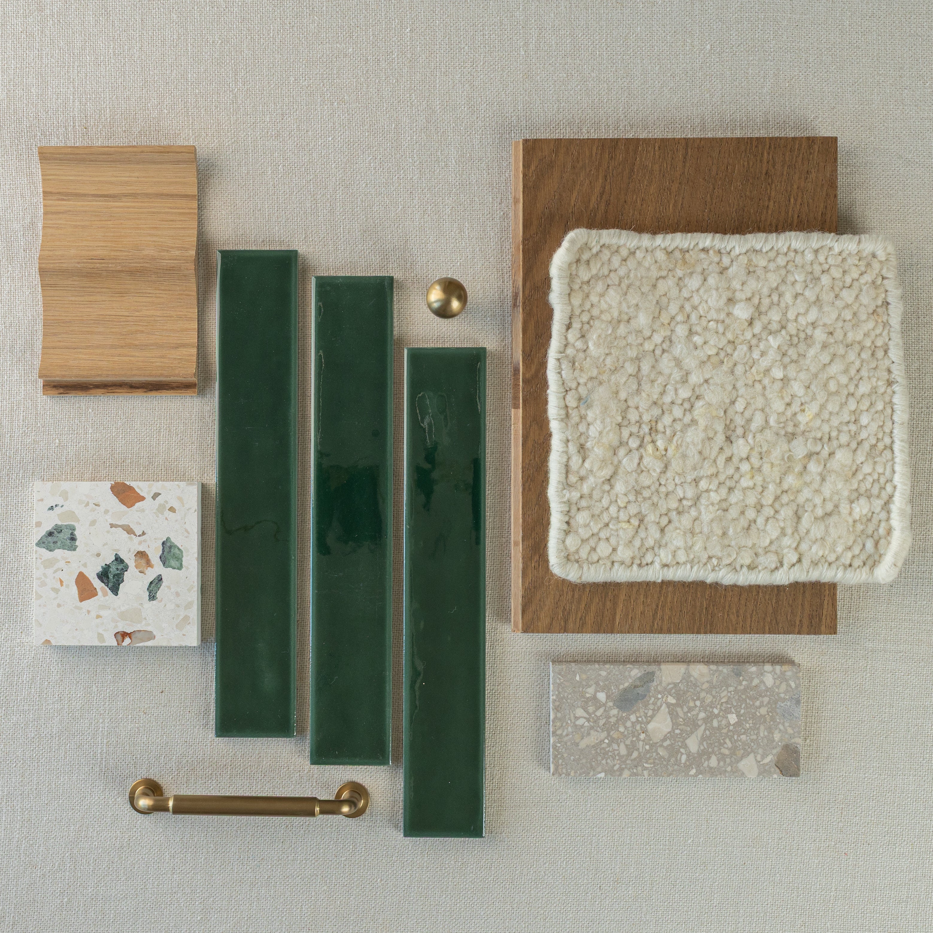 Selection of green ceramic tiles, oak wood samples, terrazzo, brass hardware, and textured cream fabric on neutral background