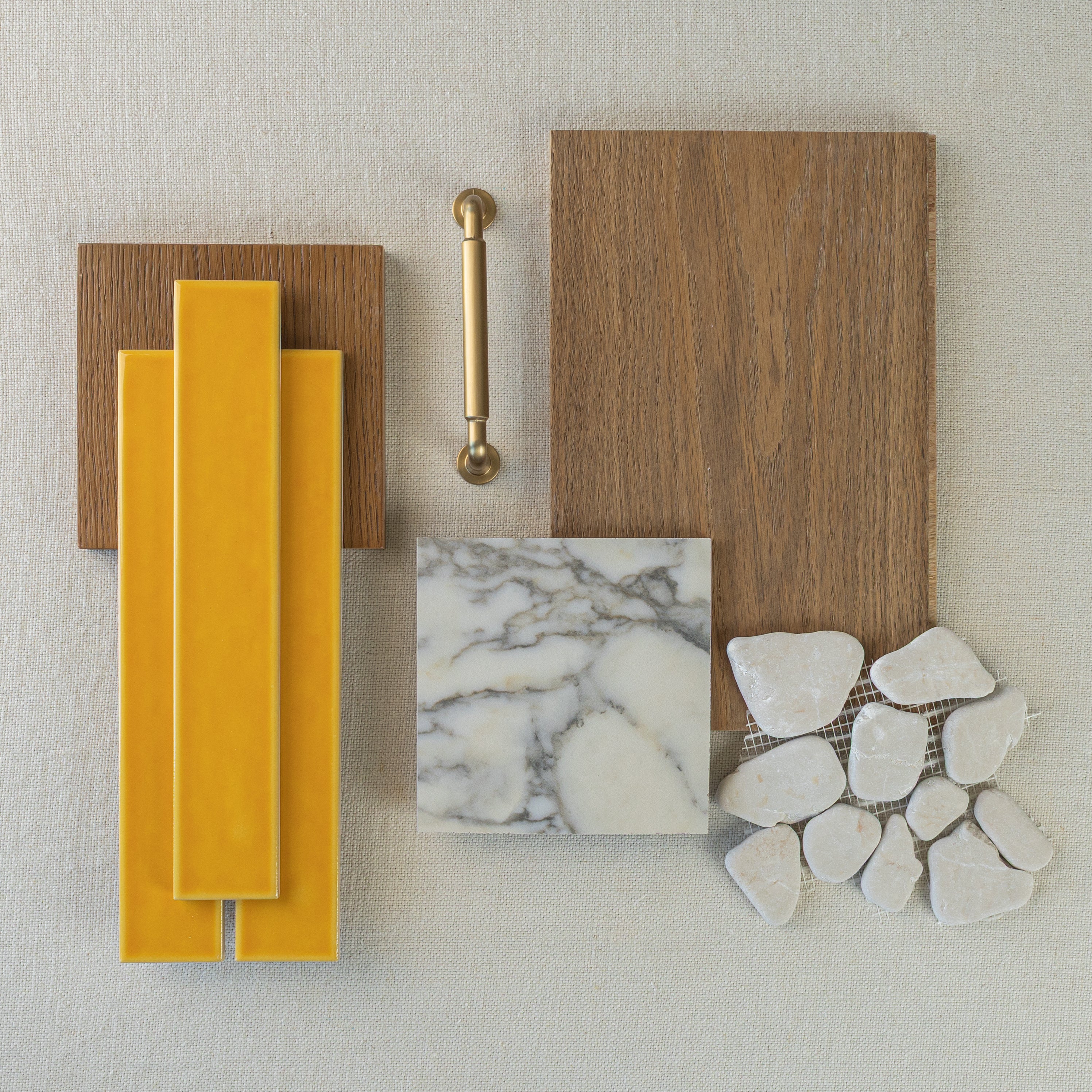 Vertical yellow ceramic tiles with wood samples, brass hardware, gray marble square, and smooth white stone pieces on fabric background