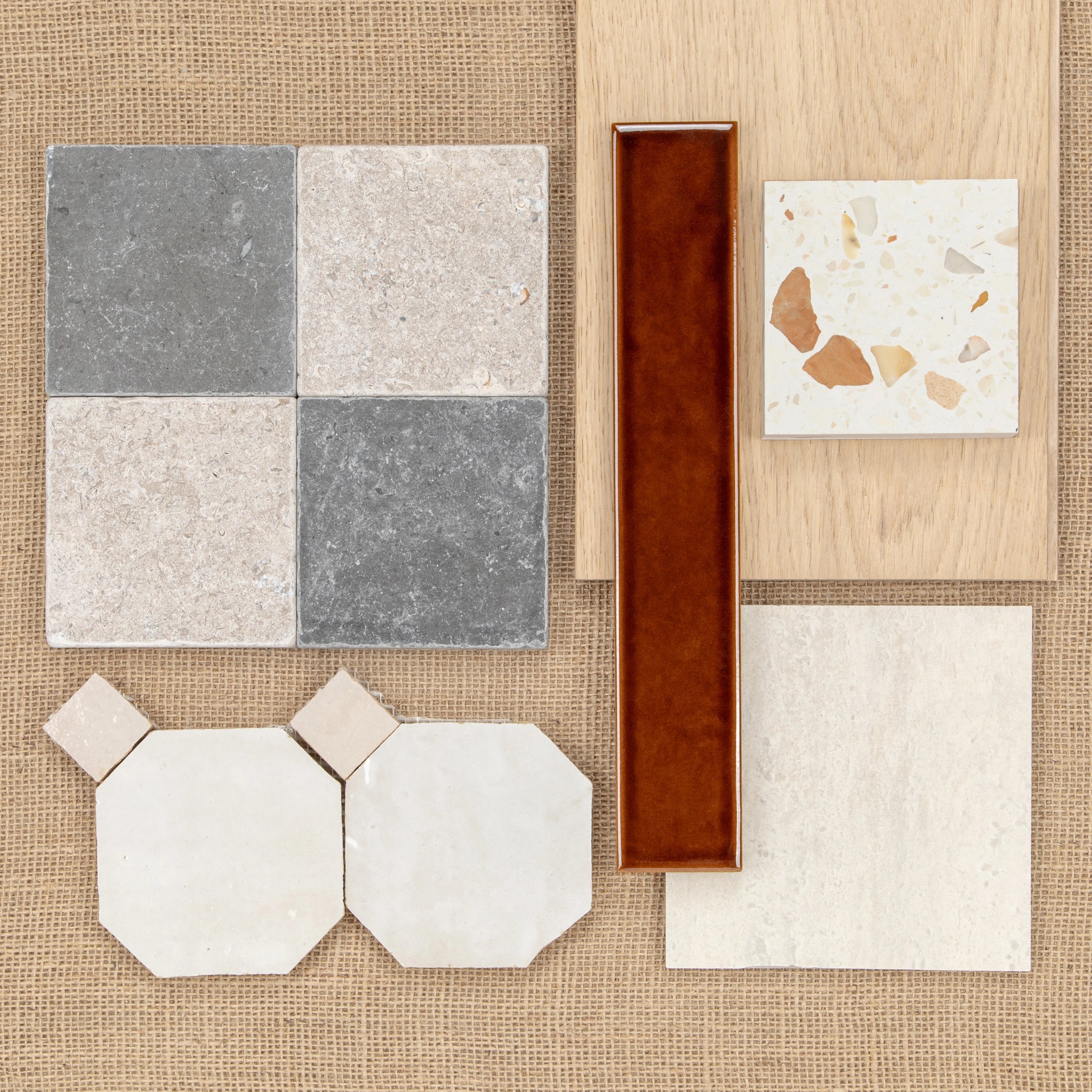 Assorted ceramic tile samples in neutral grey, beige, terracotta, and cream tones arranged on woven fabric and wood backgrounds