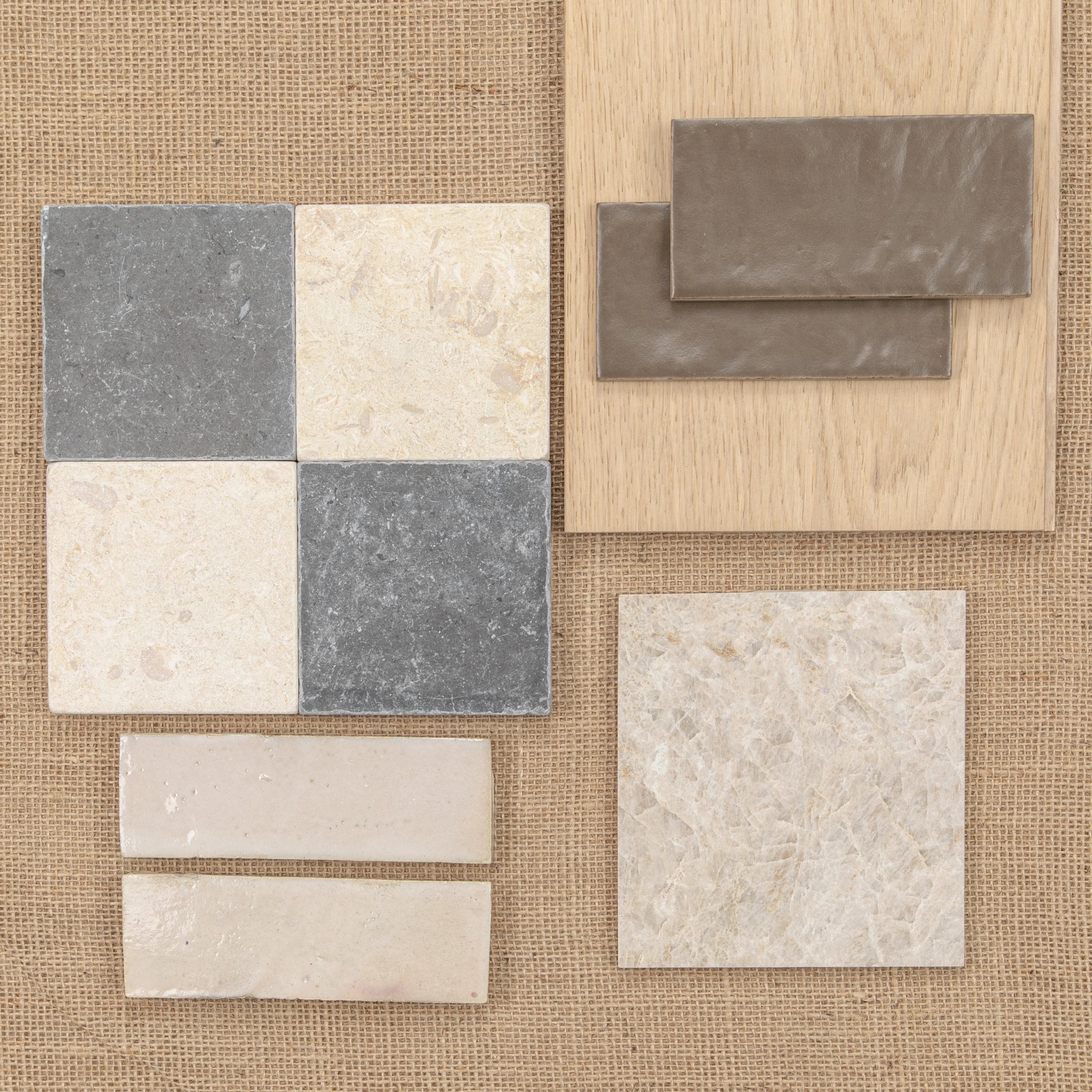 Natural stone and ceramic tile samples in soft grey, beige, and taupe shades arranged on textured fabric and wood backgrounds