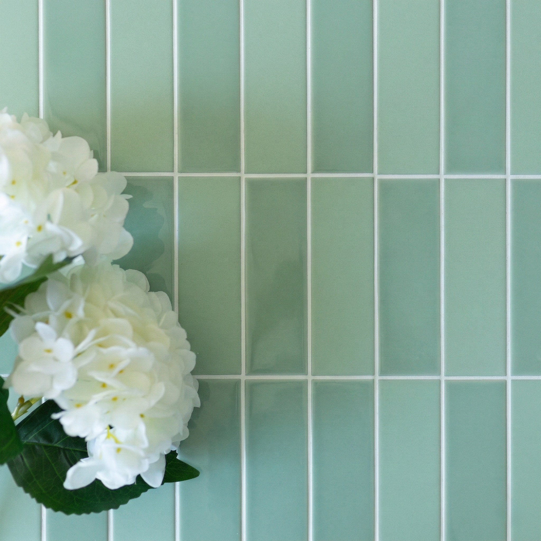 Close-up of glossy green ceramic tiles with white grout and white hydrangea flowers on the left side