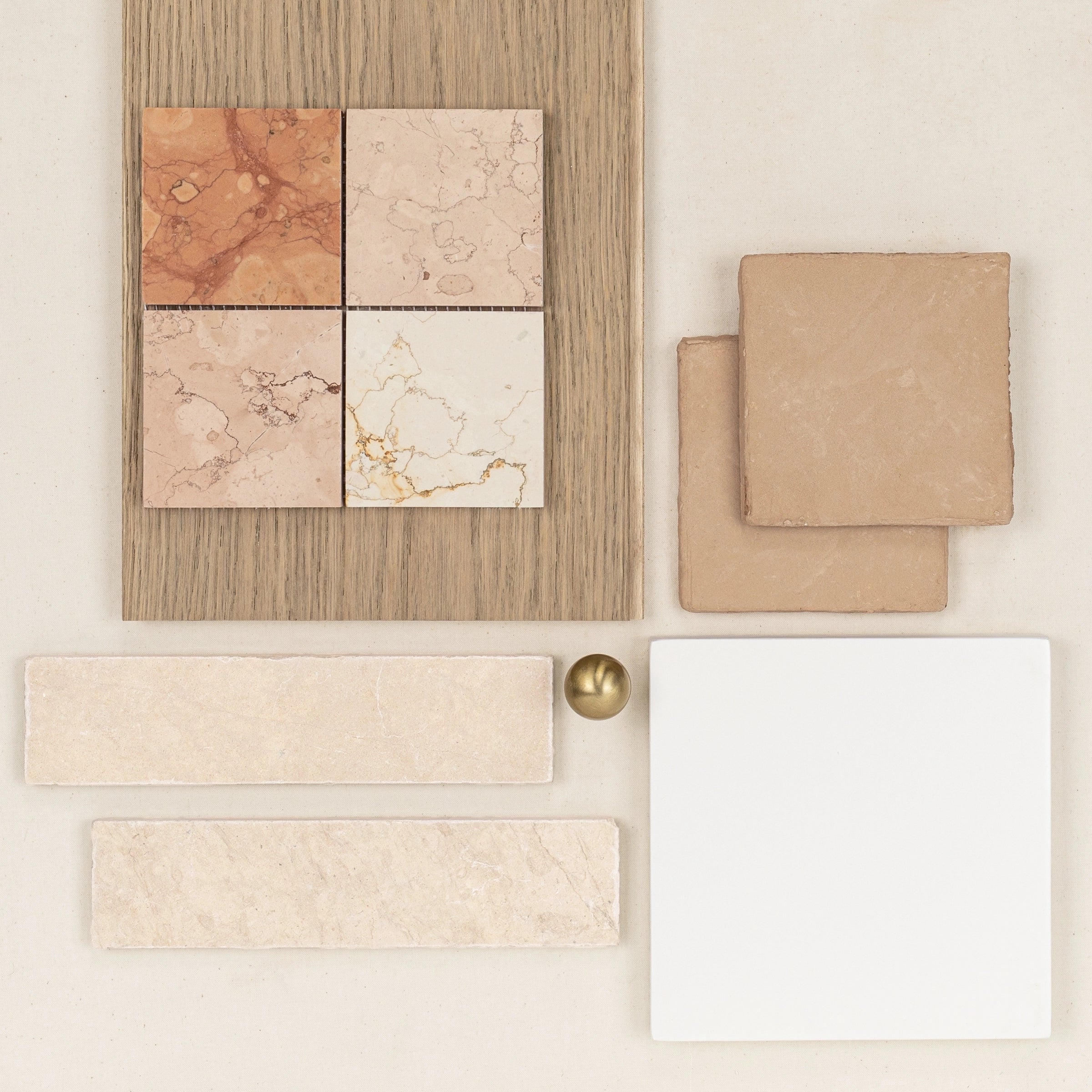 Collection of neutral ceramic tiles, wood sample, and small metallic sphere arranged on a light surface for design inspiration