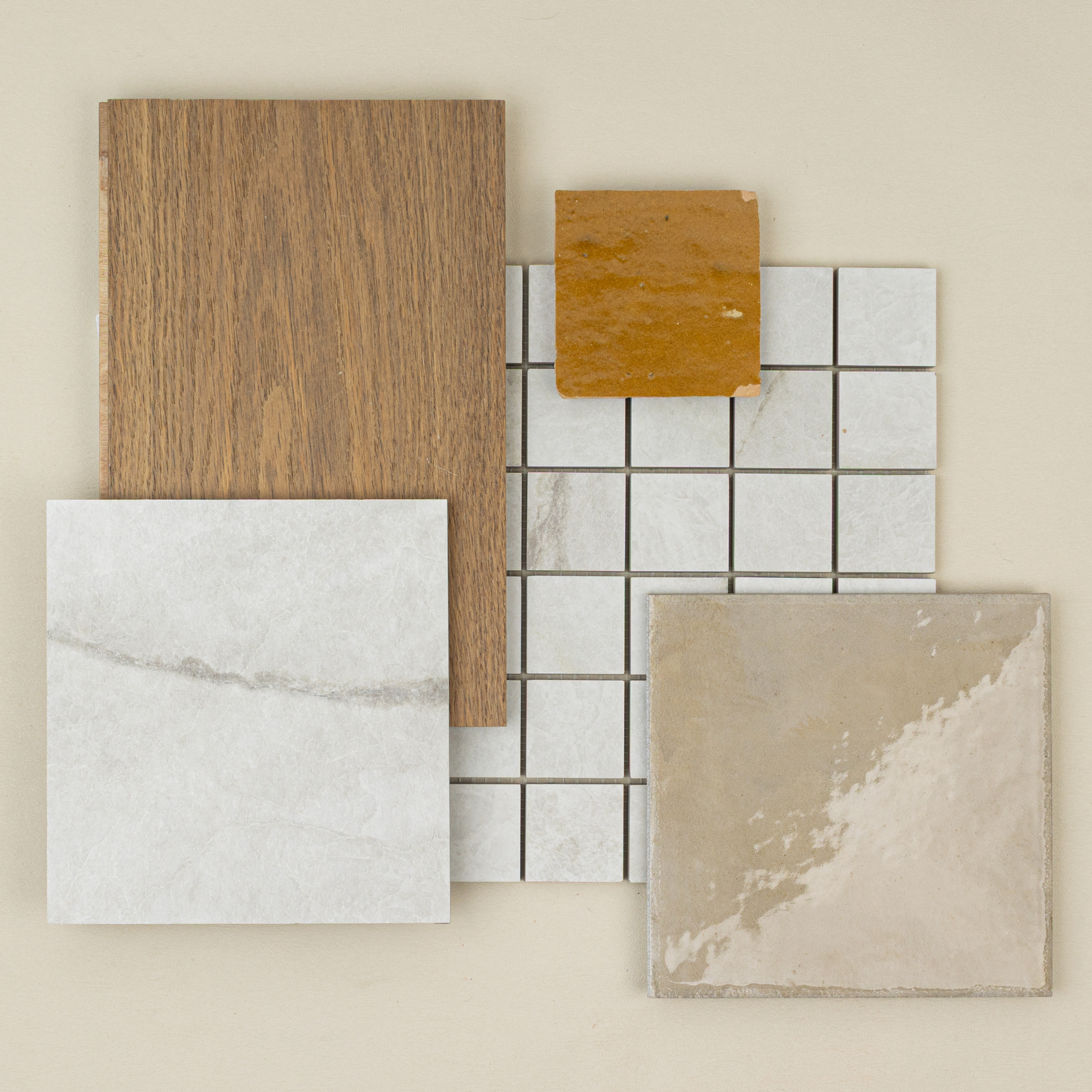 Flat lay of ceramic tiles including polished beige, matte white, small mosaic squares, wood-look sample, and mustard ceramic shard
