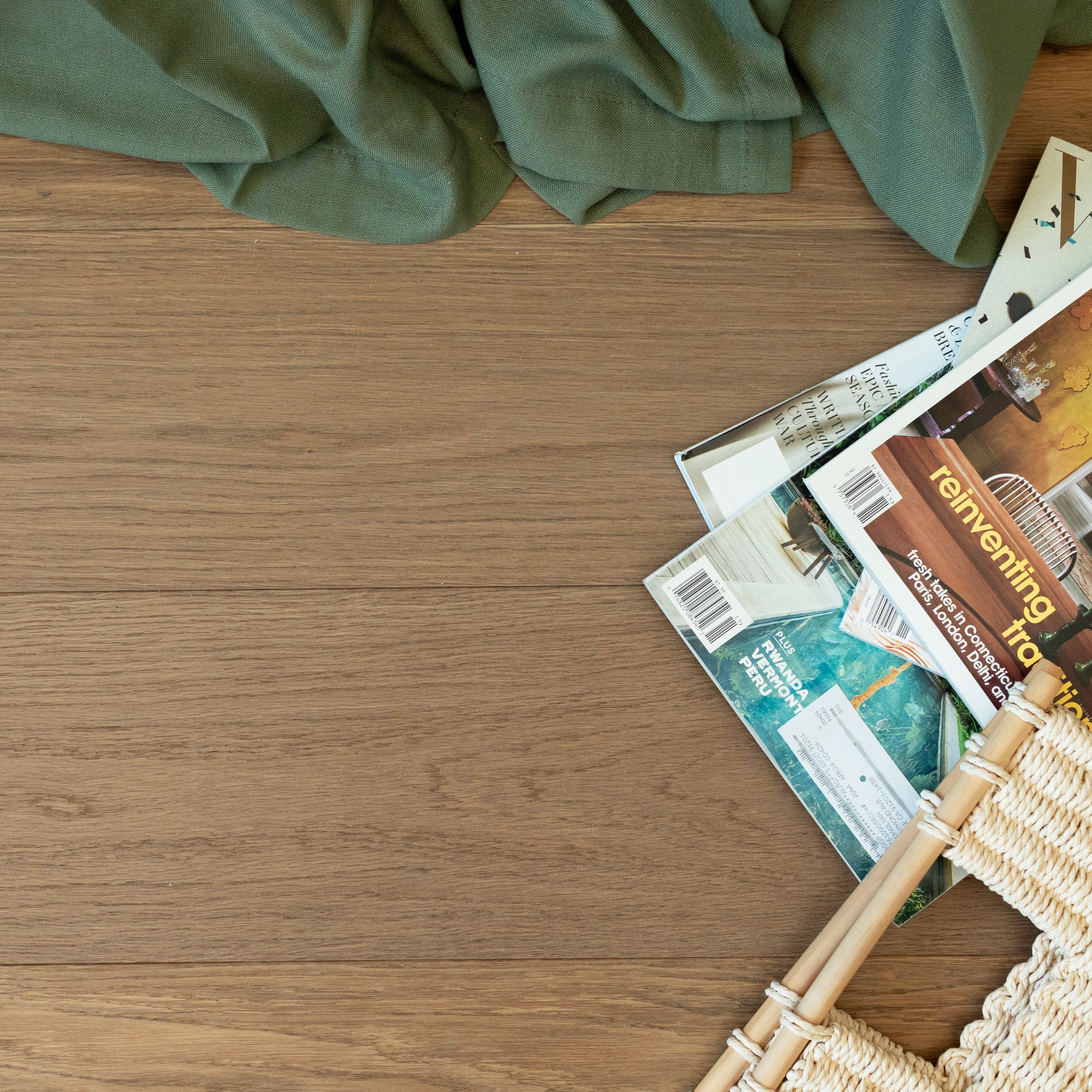 Natural oak engineered wood flooring with soft green fabric, stacked home design magazines, and woven rattan chair edge