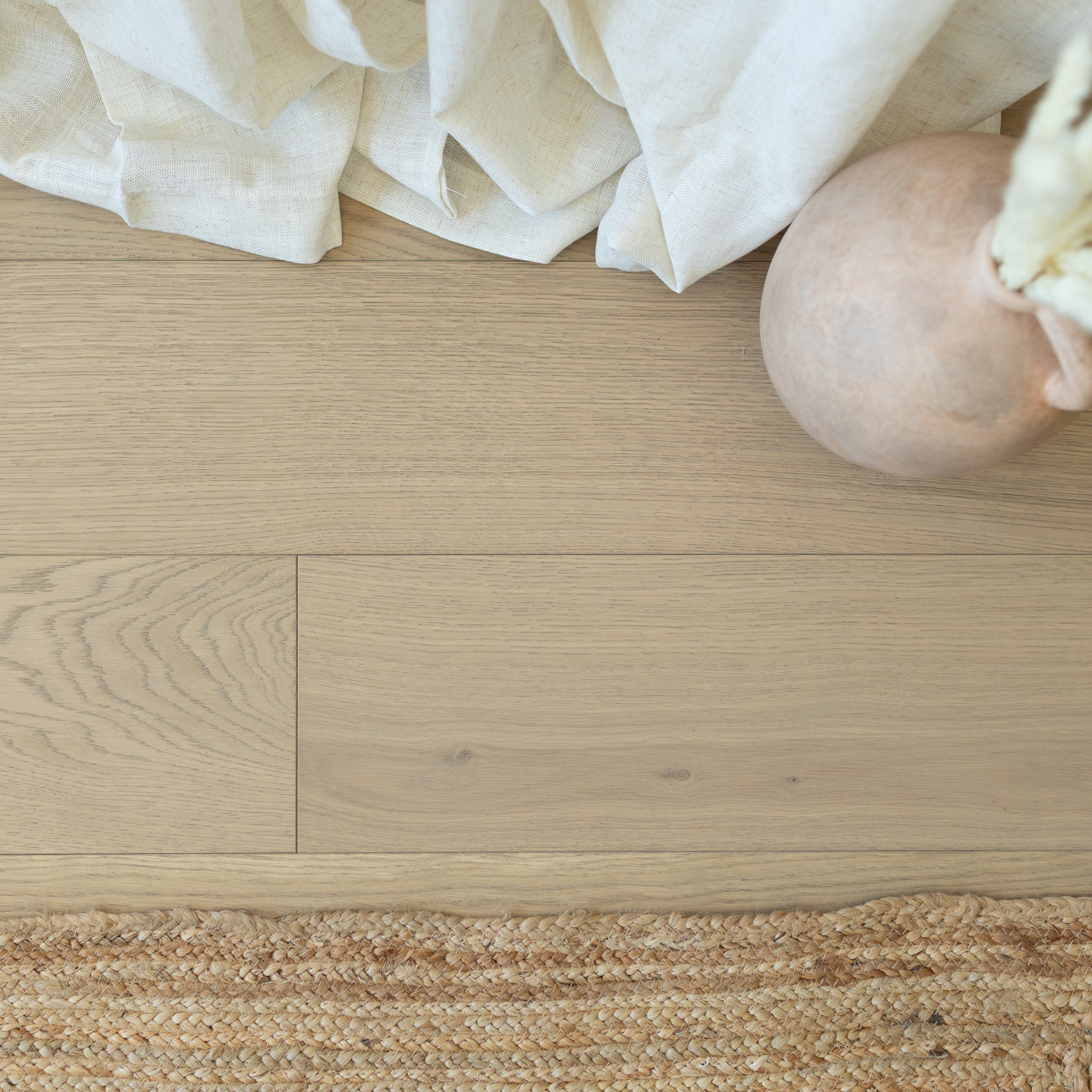 Soft light oak flooring with subtle grain, natural woven jute rug, beige linen fabric, and round clay vase edge detail