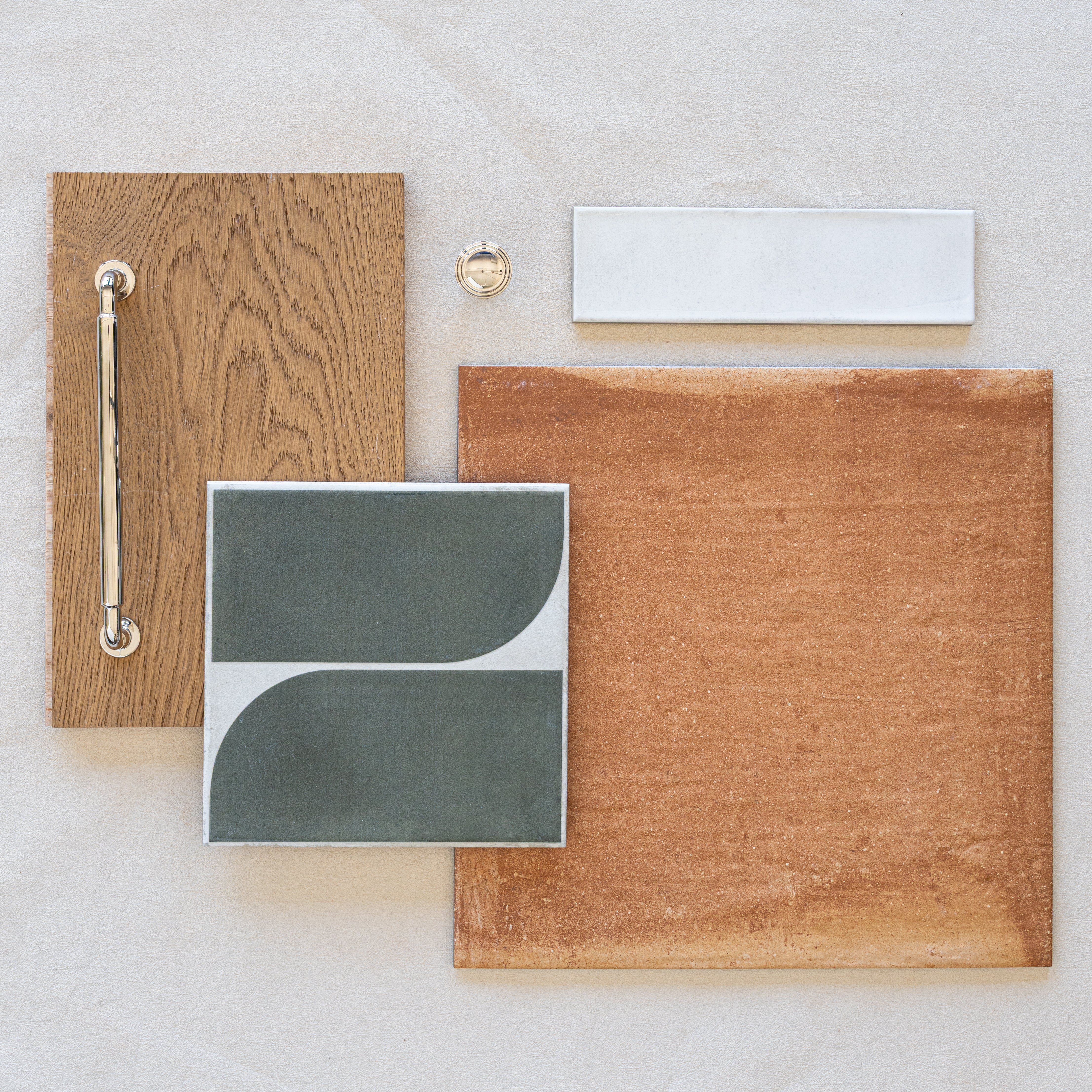 Arrangement of wood, terracotta-style tile, white and patterned ceramic tile samples with a metal handle and knob on a light fabric background