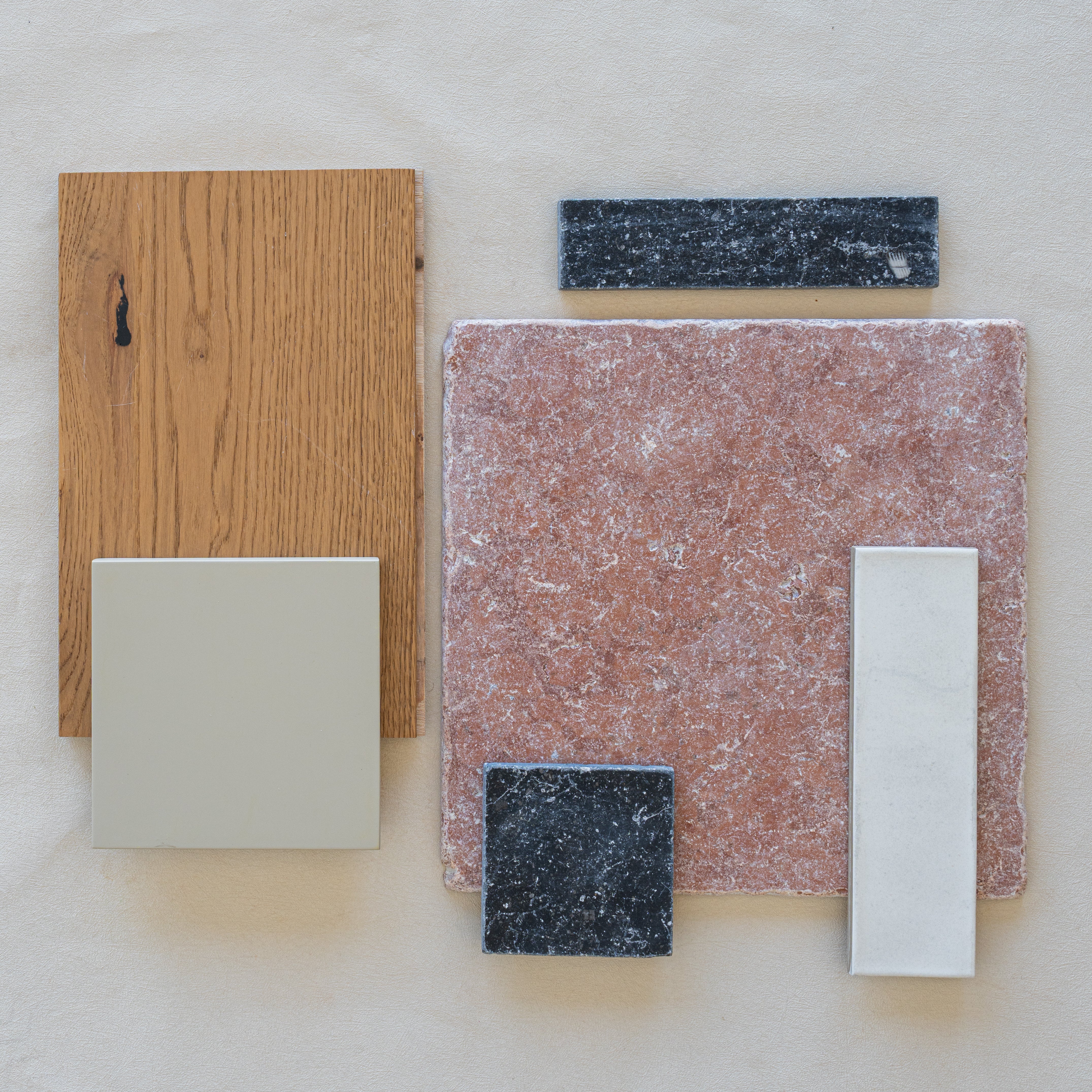 Flat lay of wood grain, mottled pink tile, smooth beige tile, and dark speckled porcelain tile samples on light surface