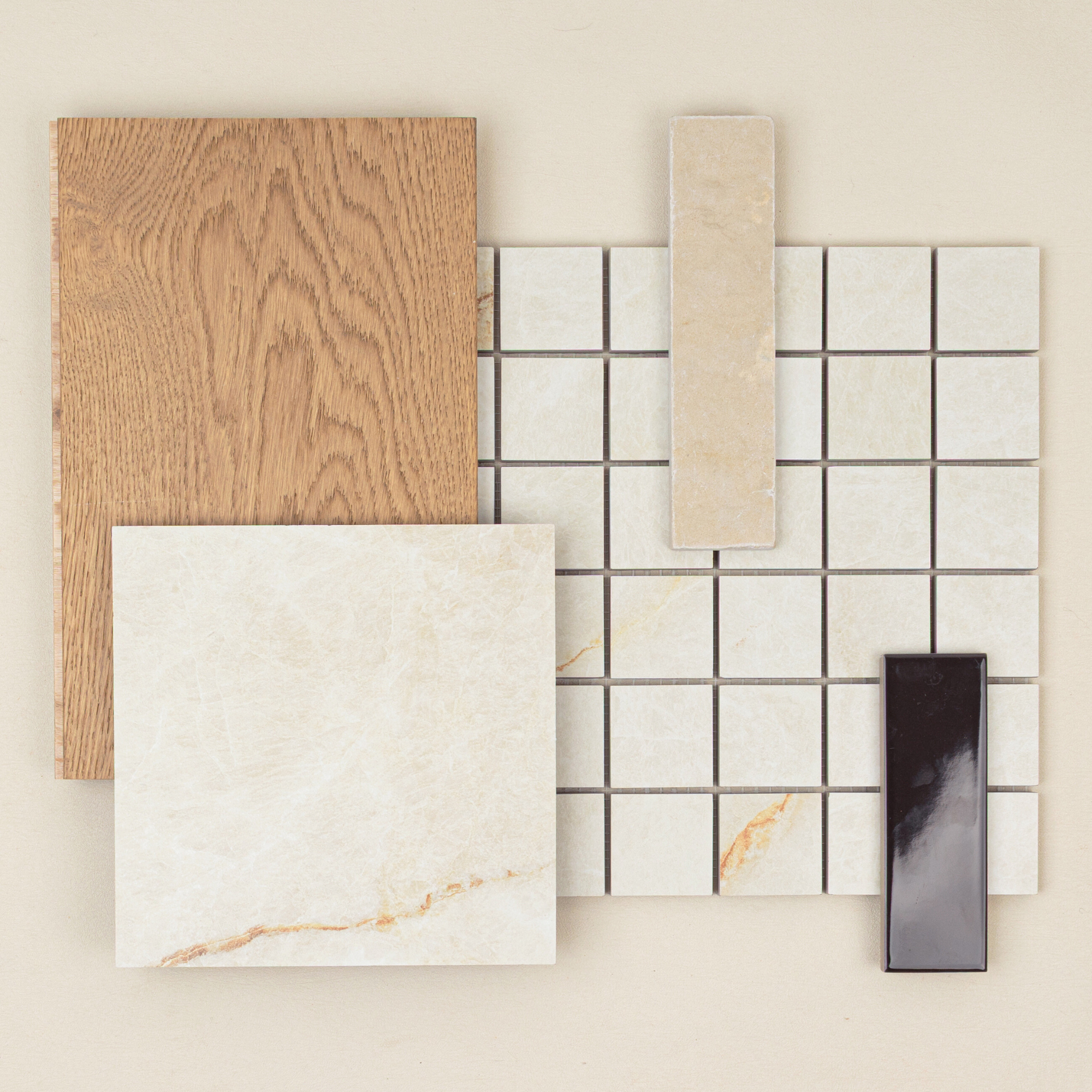 Overhead view of beige marble tile, wood plank, small cream tiles, and glossy dark rectangular tile on neutral surface