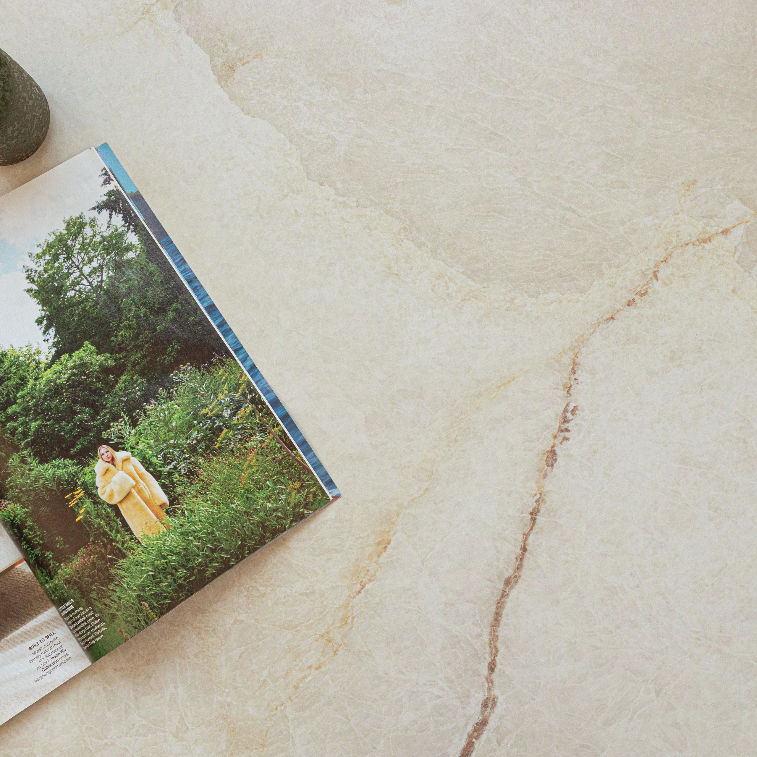 Soft beige porcelain tile surface with subtle natural veining and an open magazine featuring outdoor greenery