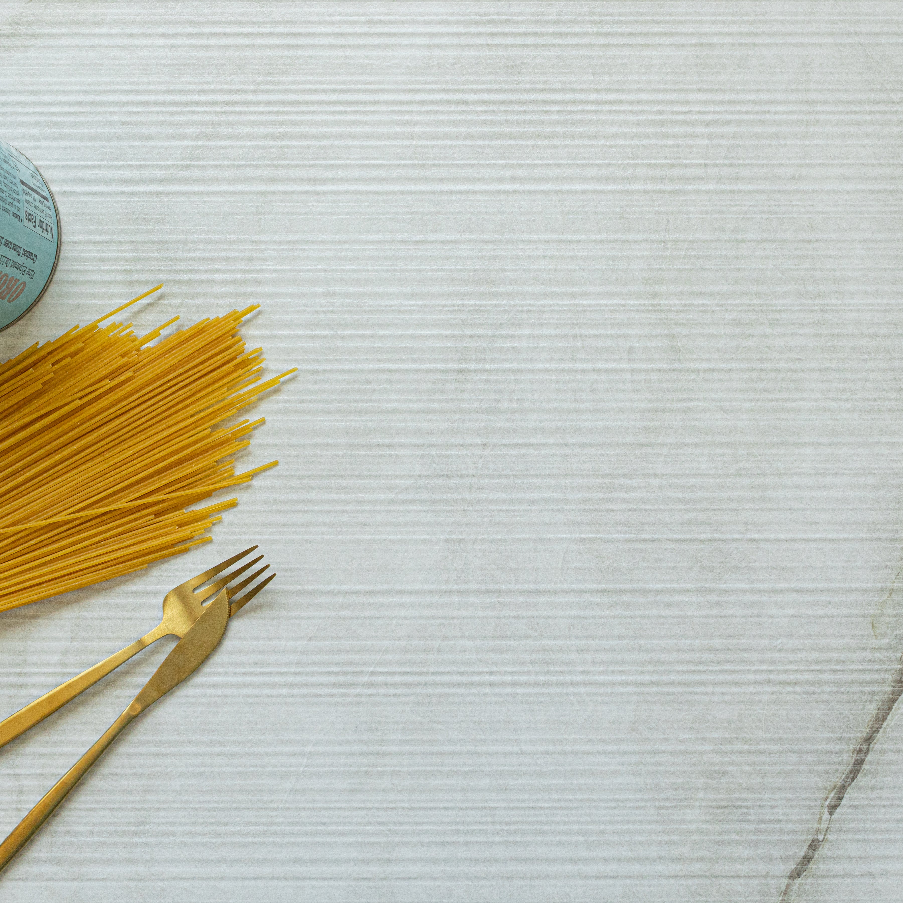 Light-colored porcelain tile with subtle striations and a soft matte finish shown with uncooked spaghetti and gold flatware on the side