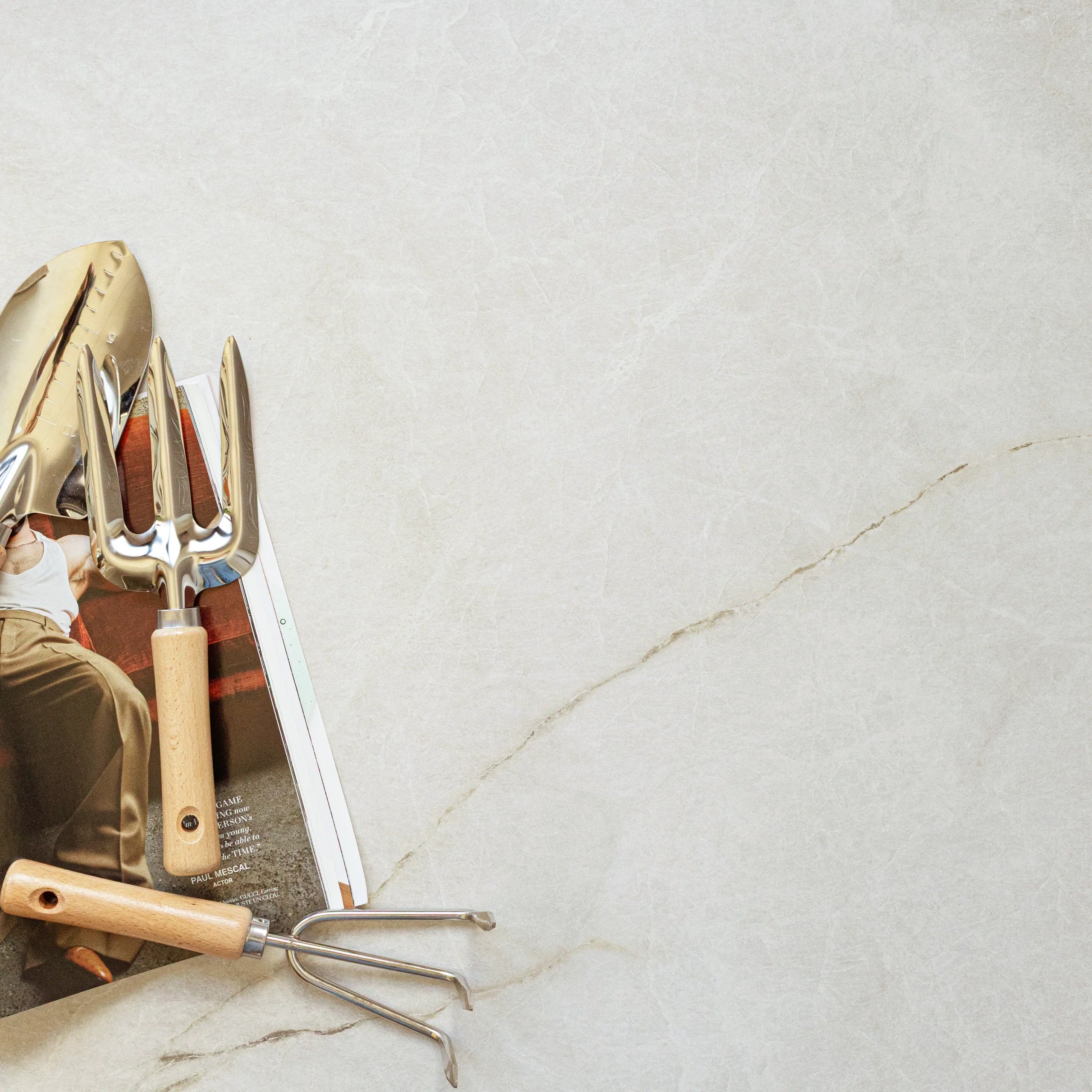 Creamy porcelain tile surface with fine natural veining and gardening tools resting on an open magazine page