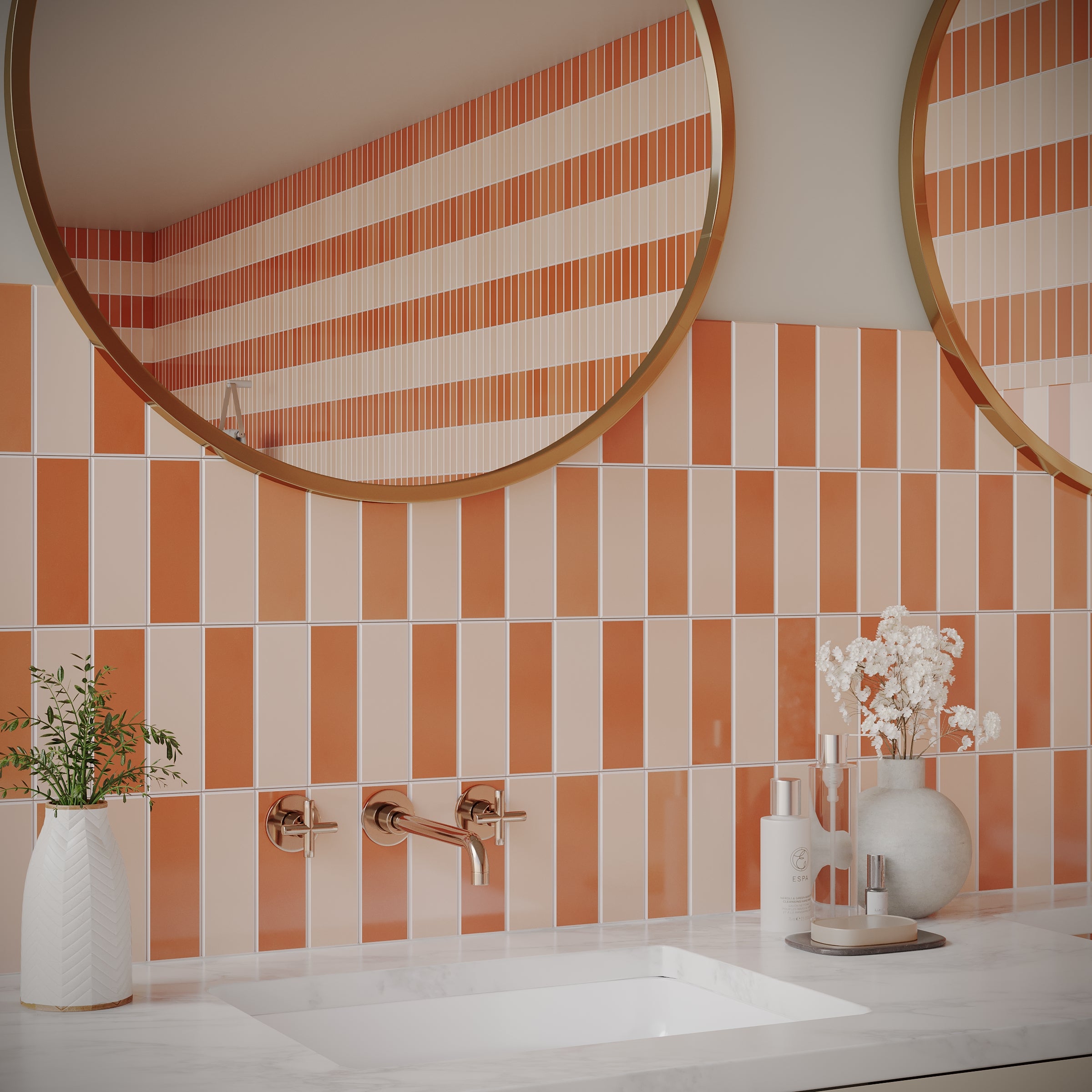 Bathroom vanity with two round mirrors above orange and white vertical striped ceramic tiles and decorative vases on countertop