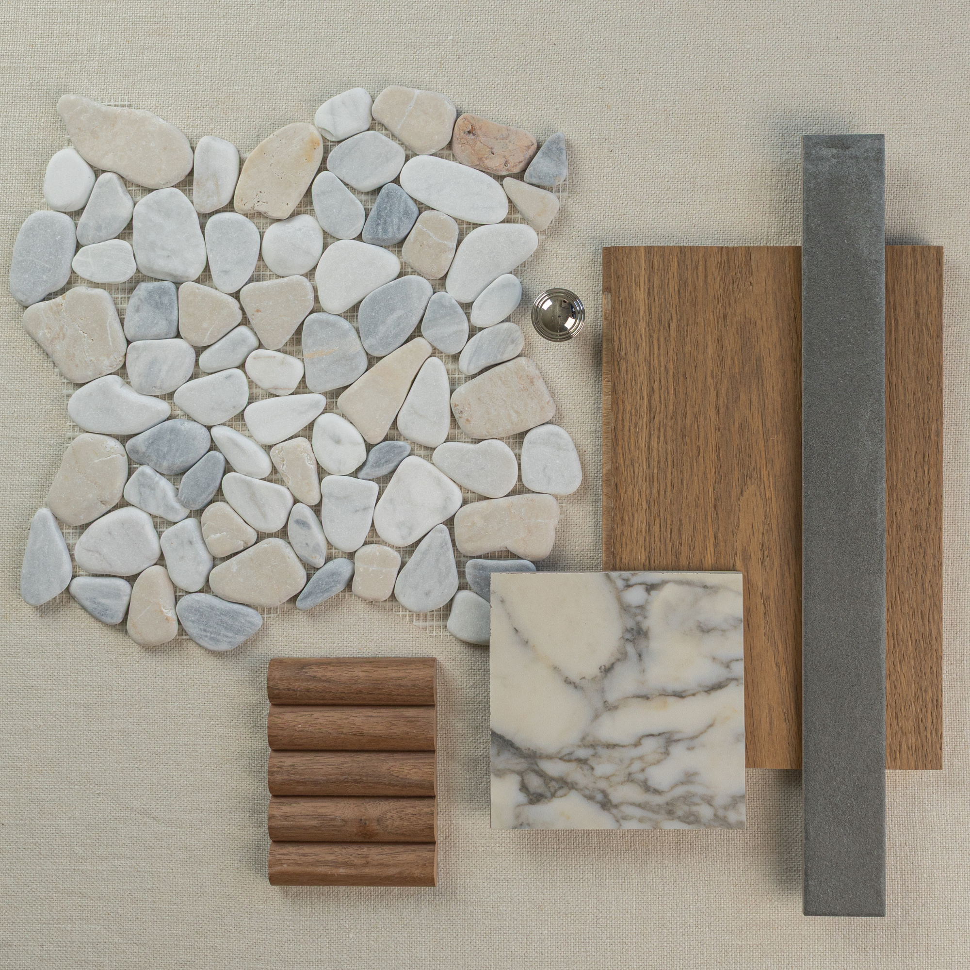 Flat lay of irregular light stone pebbles, wood samples, marble, gray rectangular tile, and metal knob on beige surface