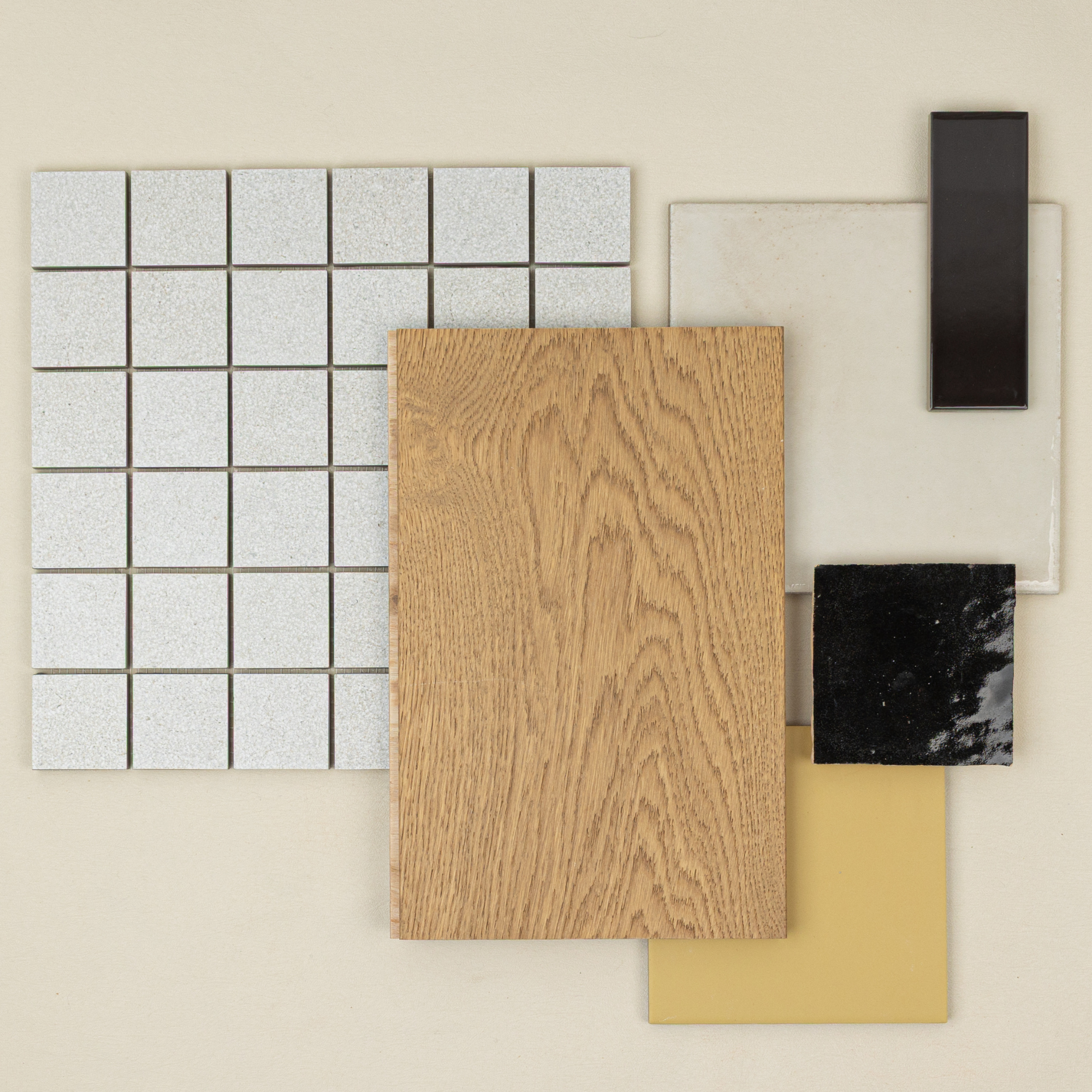 Flat lay of wood sample with beige, black, clear, mustard, and light gray square tile swatches on neutral background
