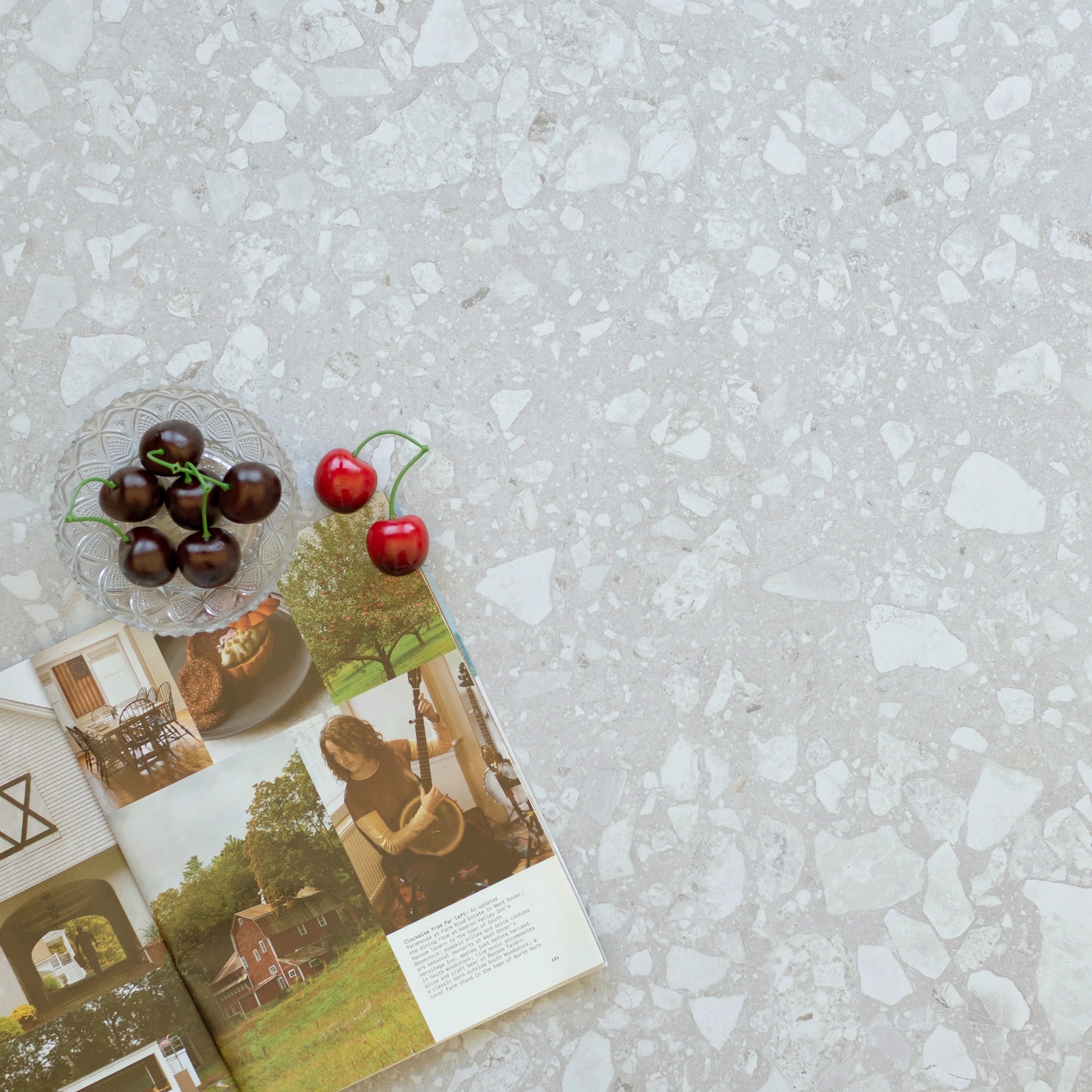 Gray terrazzo surface with white stone chips, featuring a small bowl of cherries and an open lifestyle magazine nearby