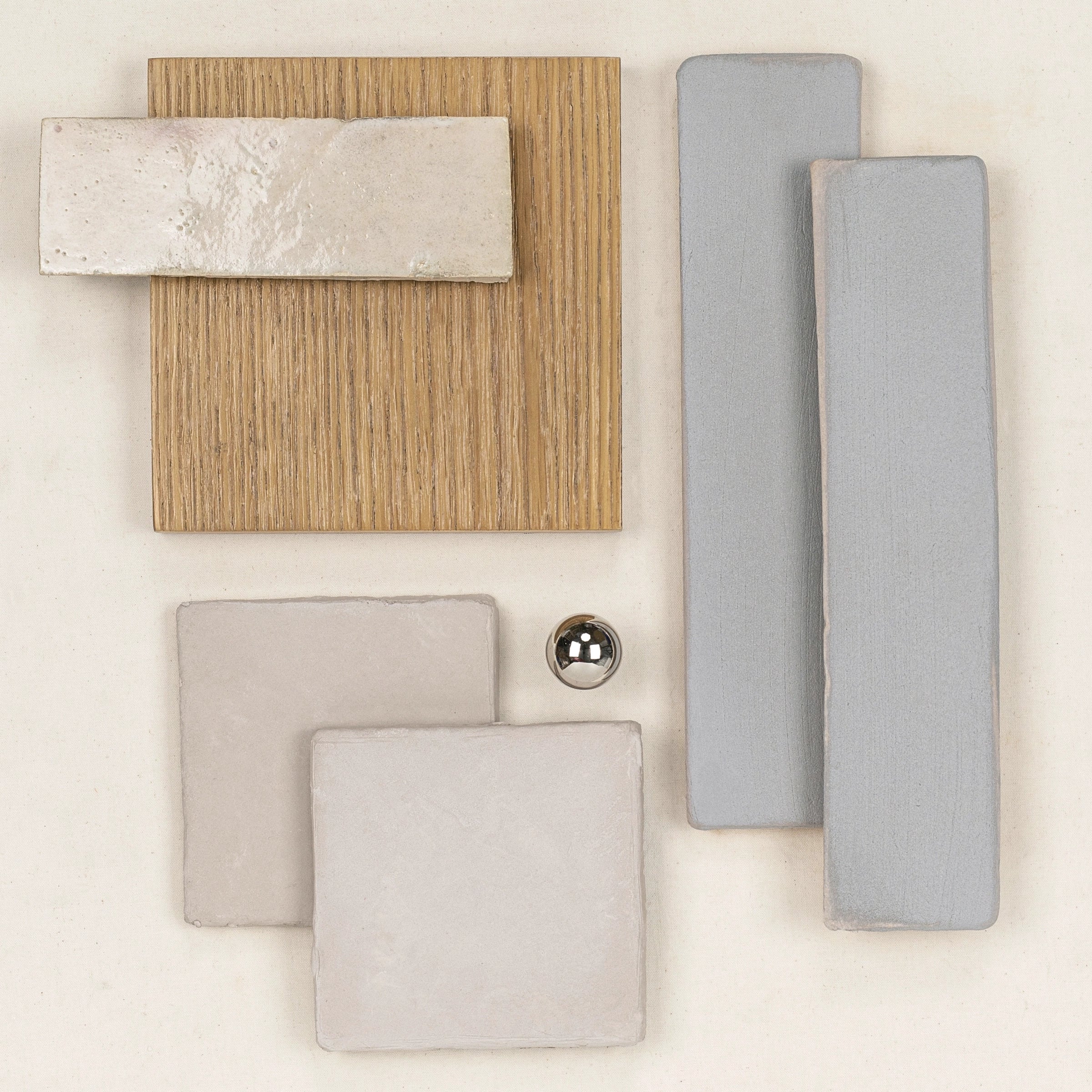 Assortment of neutral-toned ceramic tiles and wood sample with a small metallic sphere on a light background