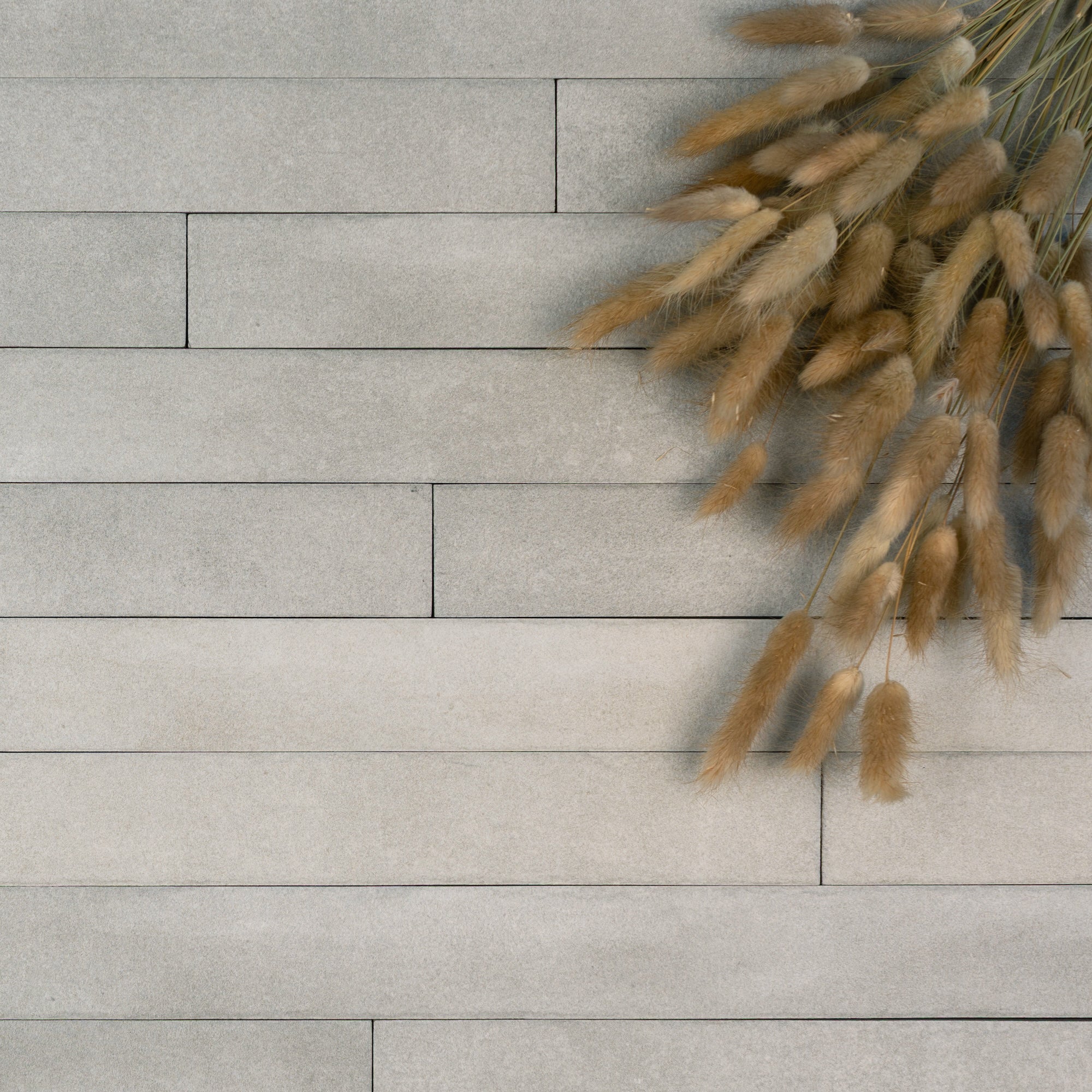 Light gray rectangular ceramic tiles arranged in a staggered pattern with a bundle of beige dried ornamental grass in the corner