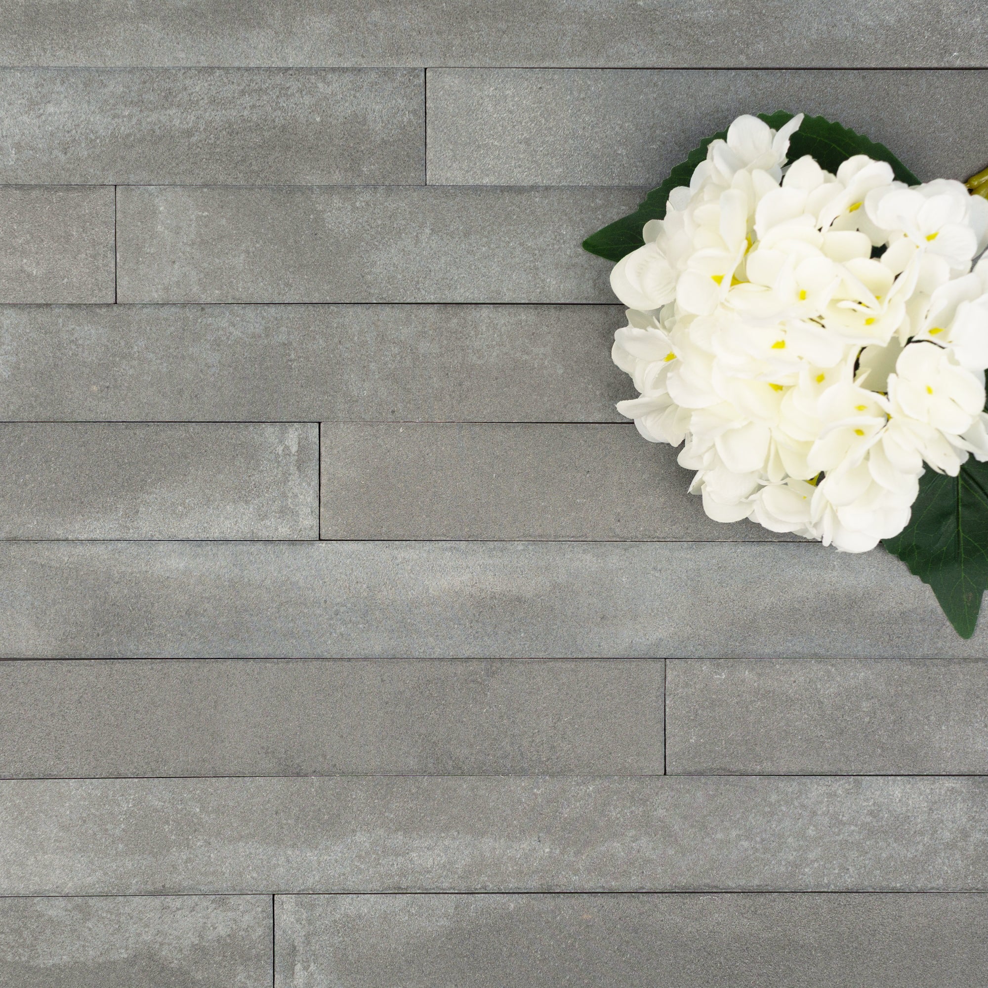 Matte gray ceramic tiles arranged horizontally with a cluster of white hydrangea flowers and green leaves in the corner