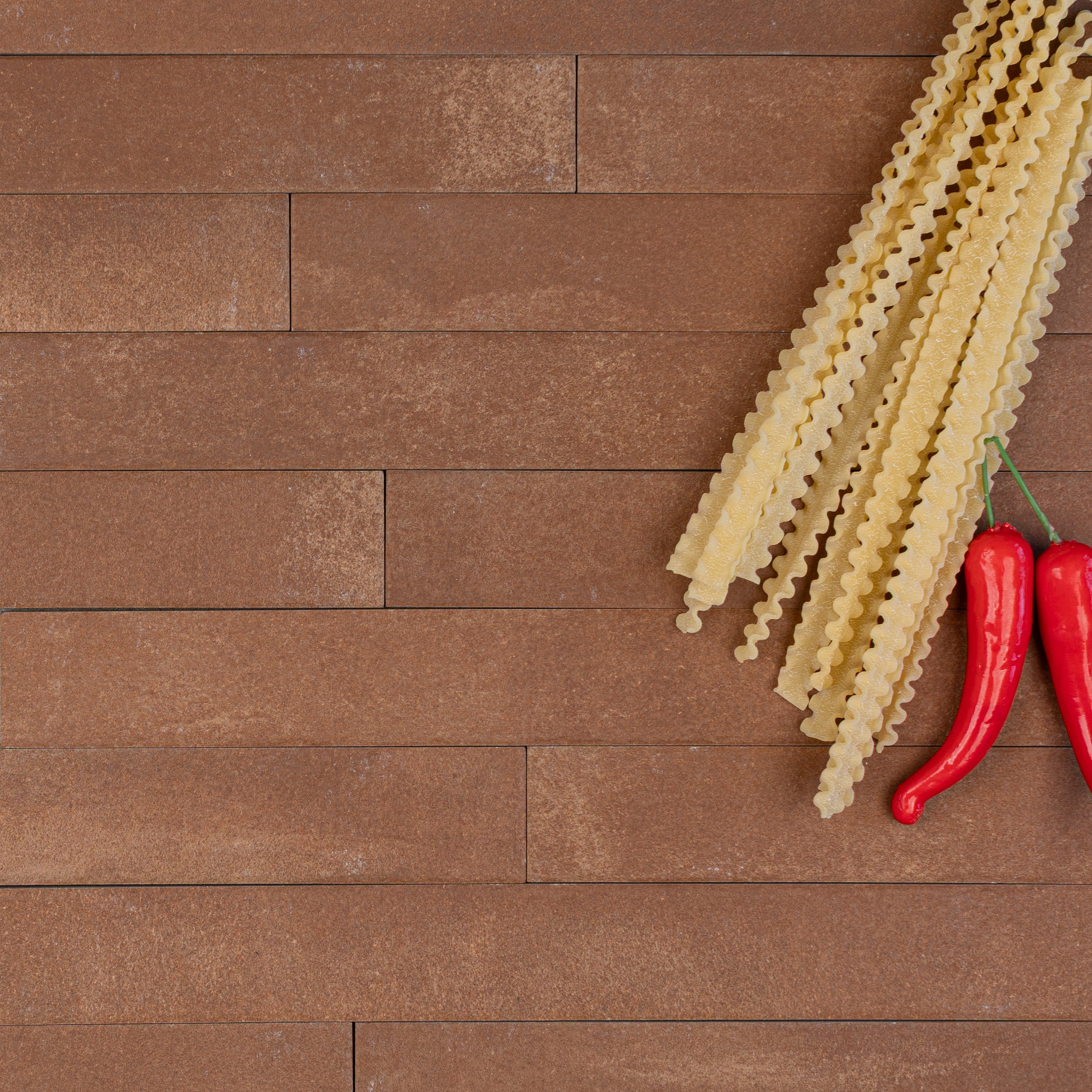 Matte terracotta rectangular tiles arranged horizontally with dried pasta strips and two red chili peppers on the side