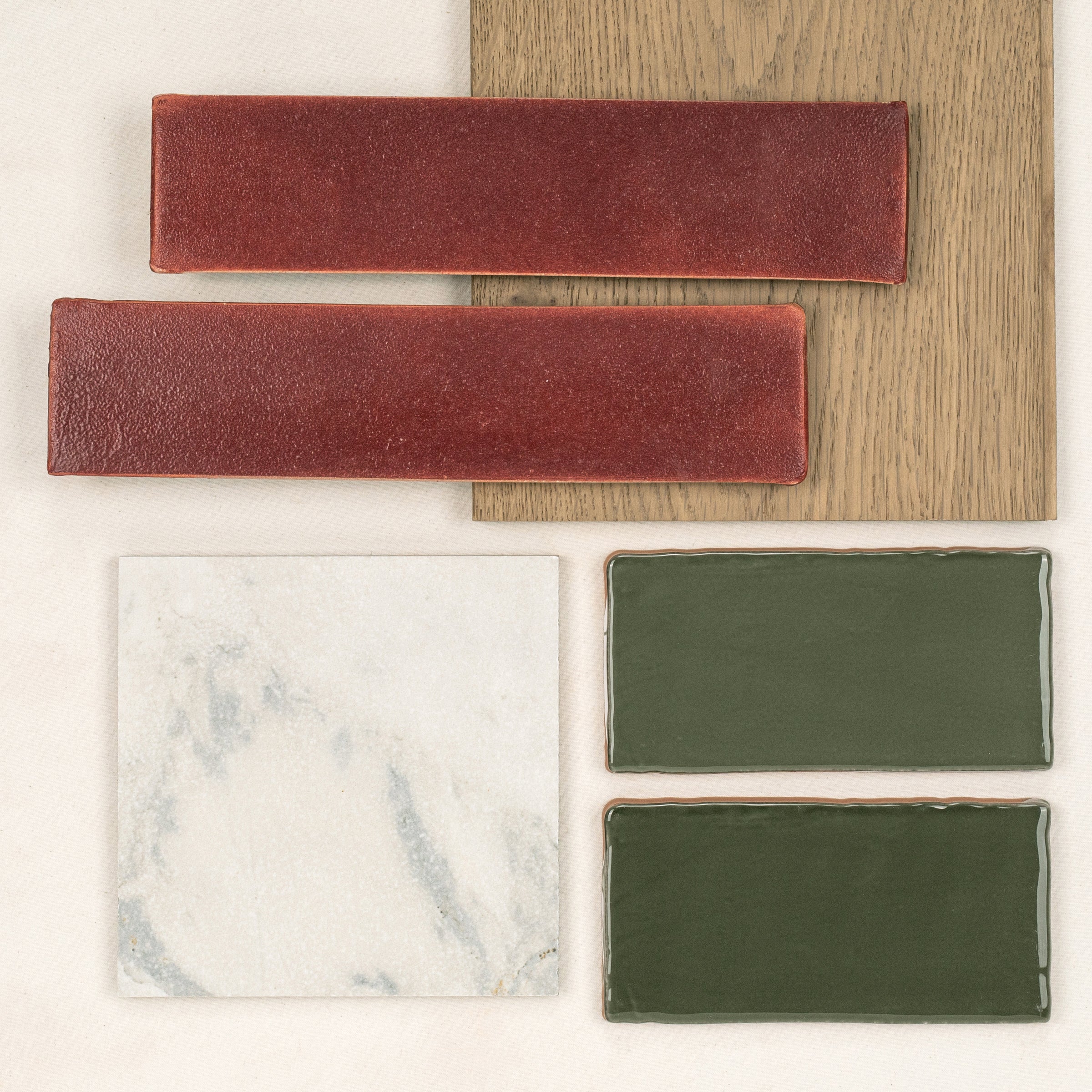 Arrangement of rustic red terracotta tiles, olive green ceramic tiles, marble-look square tile, and natural oak wood sample on pale background