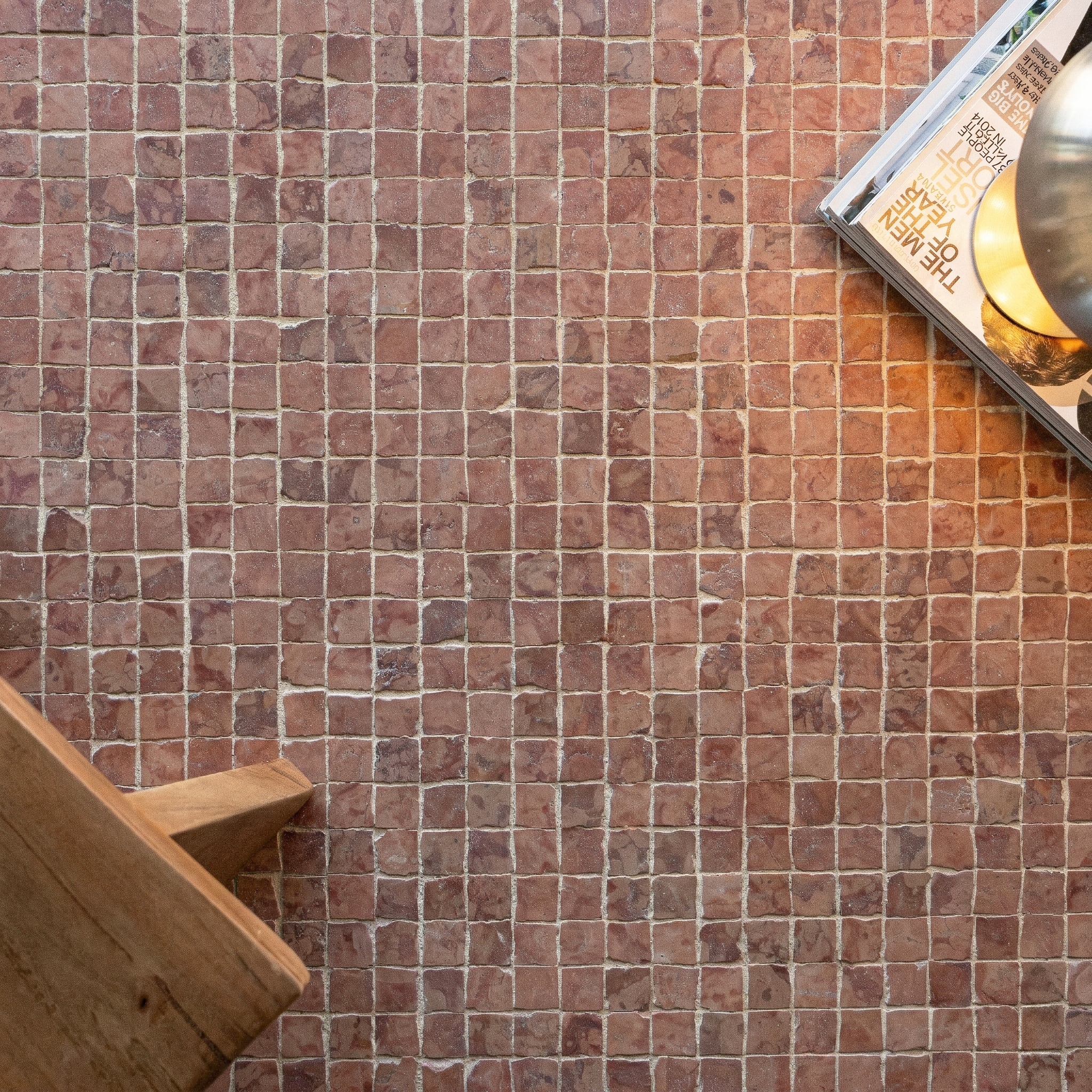Square hand-chipped terracotta tiles in warm reddish tones with textured surface and natural grout lines nearby wooden chair and book stack