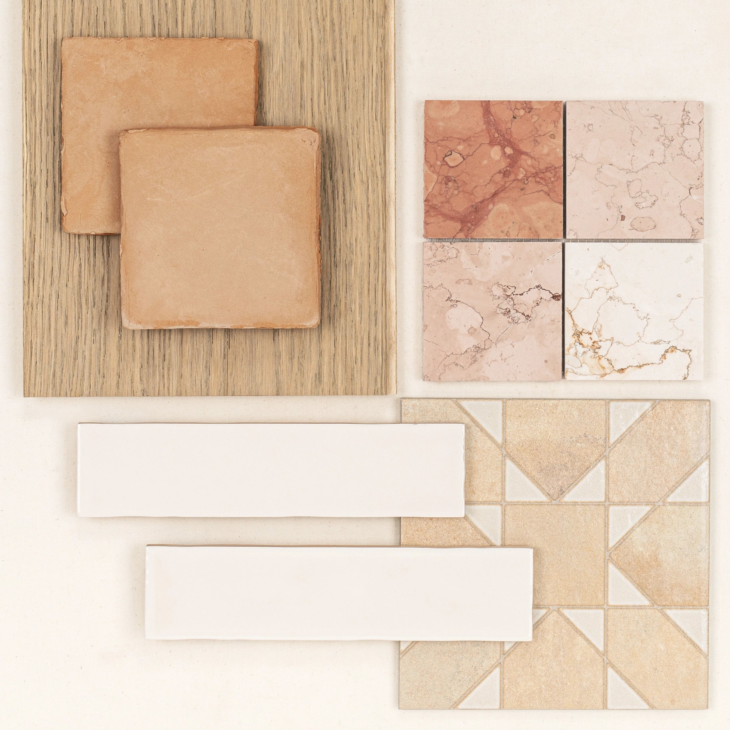 Selection of natural stone and ceramic tiles in warm beige and soft pink tones arranged on light wood and white surfaces
