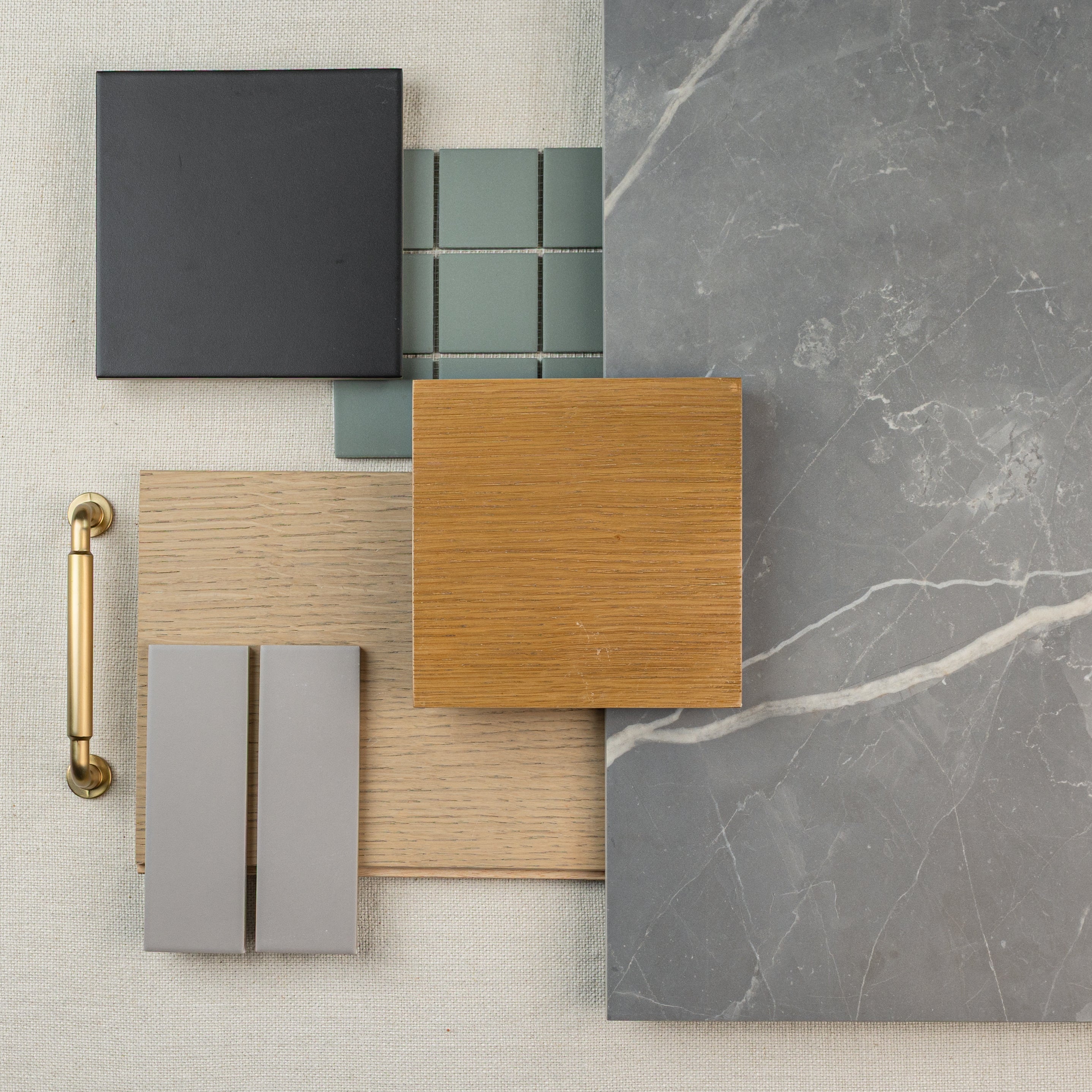 Flat lay of various material samples including black and gray tiles, wood finishes, brass handle, and large gray marble surface