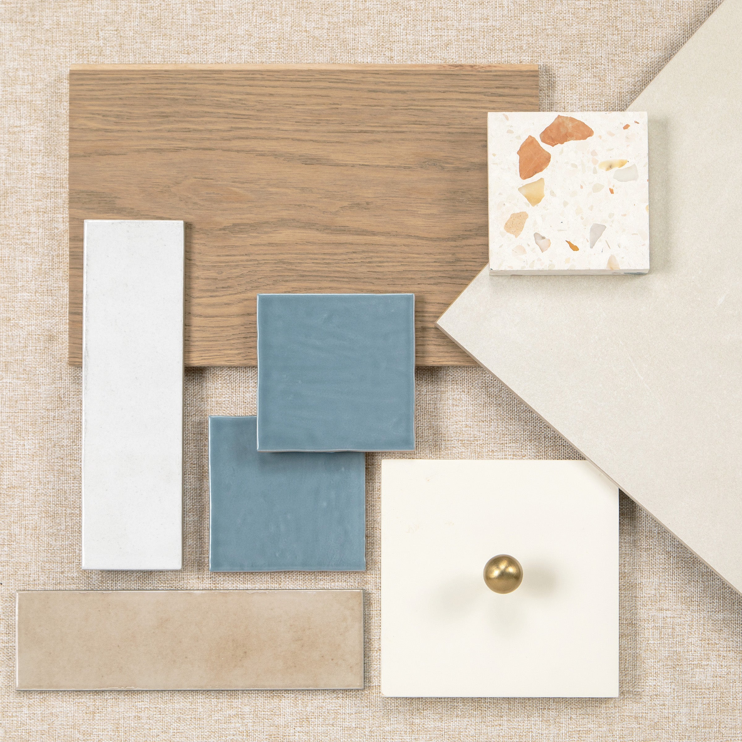 Flat lay of wood flooring and assorted tile samples with a white cabinet door and brass knob