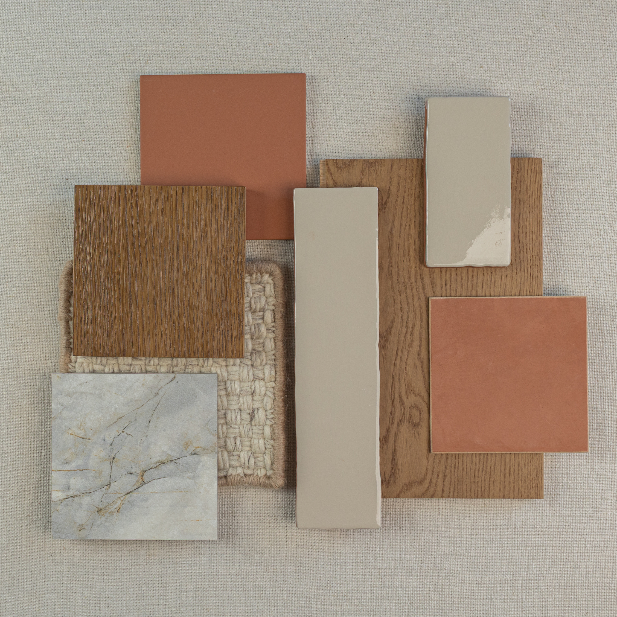 Flat lay of terracotta, beige, wood grain, marble-look porcelain tiles, and woven neutral fabric swatches on a light background