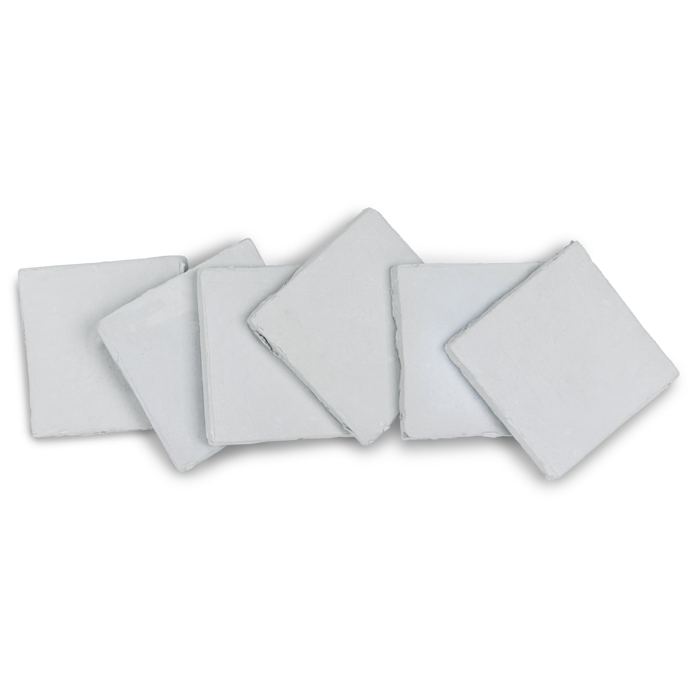 Arrangement of six pale grey ceramic tiles with uneven edges on a white surface highlighting texture and shape
