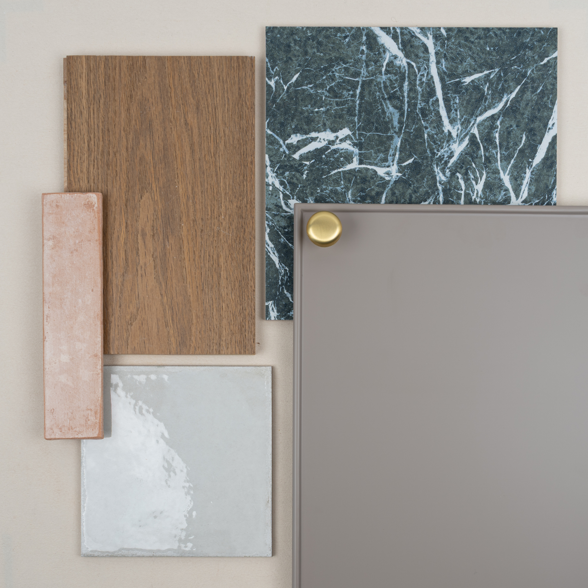 Flat lay of wood, terracotta, gray marble, glossy ceramic tile, and matte gray panel with brass knob on neutral background